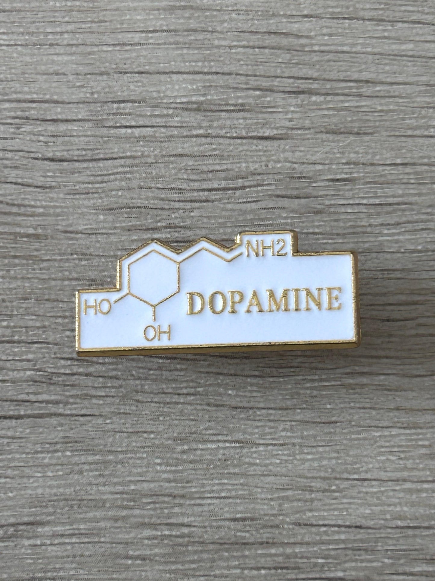 Broche rectangulaire émail blanche, contour doré, texte DOPAMINE, symboles HO et NH2.