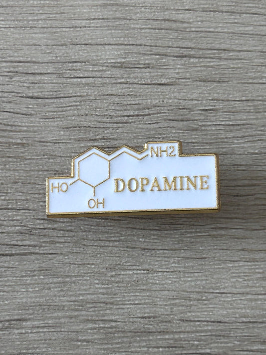Broche rectangulaire émail blanche, contour doré, texte DOPAMINE, symboles HO et NH2.
