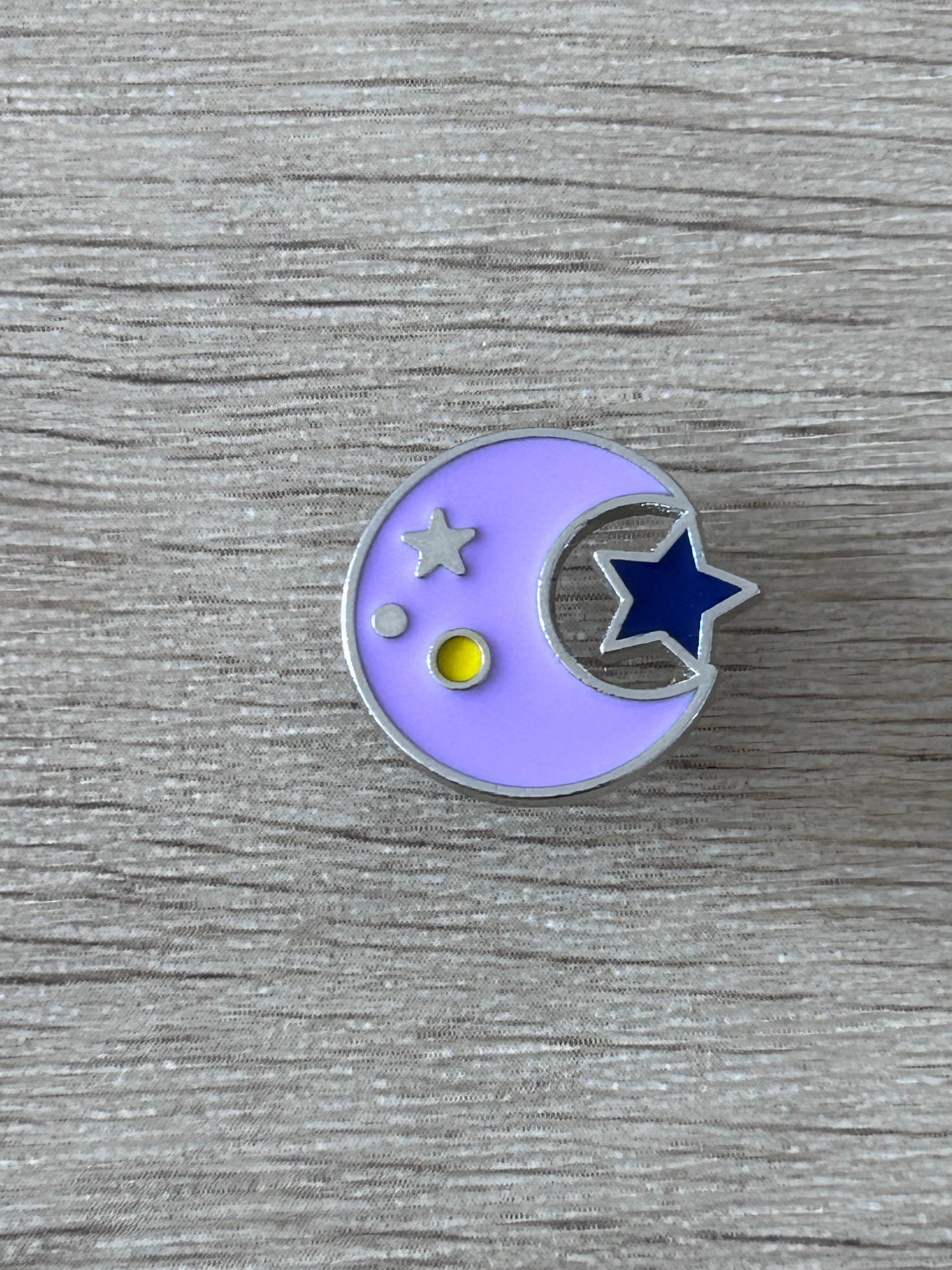 Pin's rond lilas avec lune et étoiles, petit point jaune.