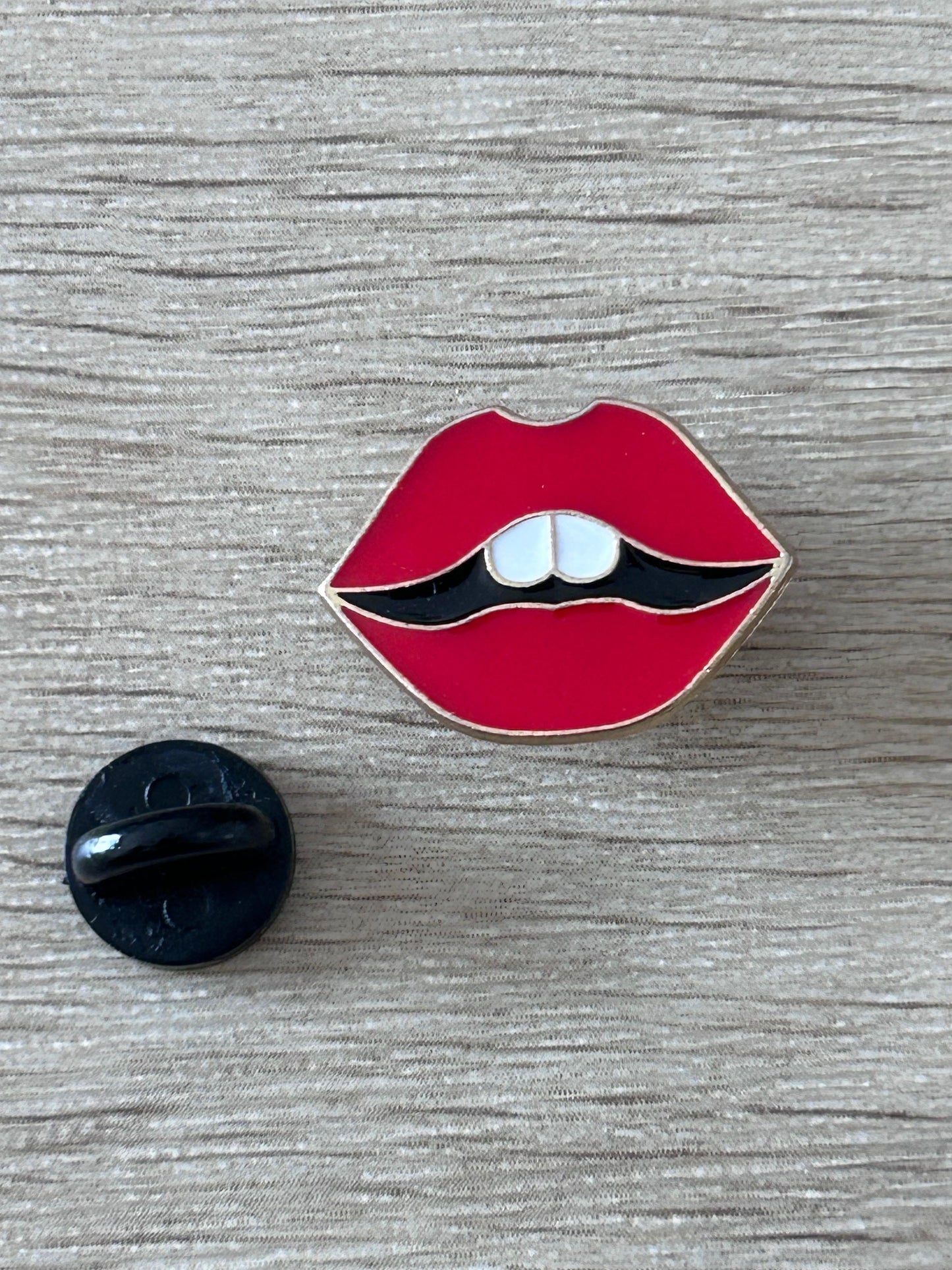 Épingle en forme de lèvres rouges, dents blanches visibles et contour noir.