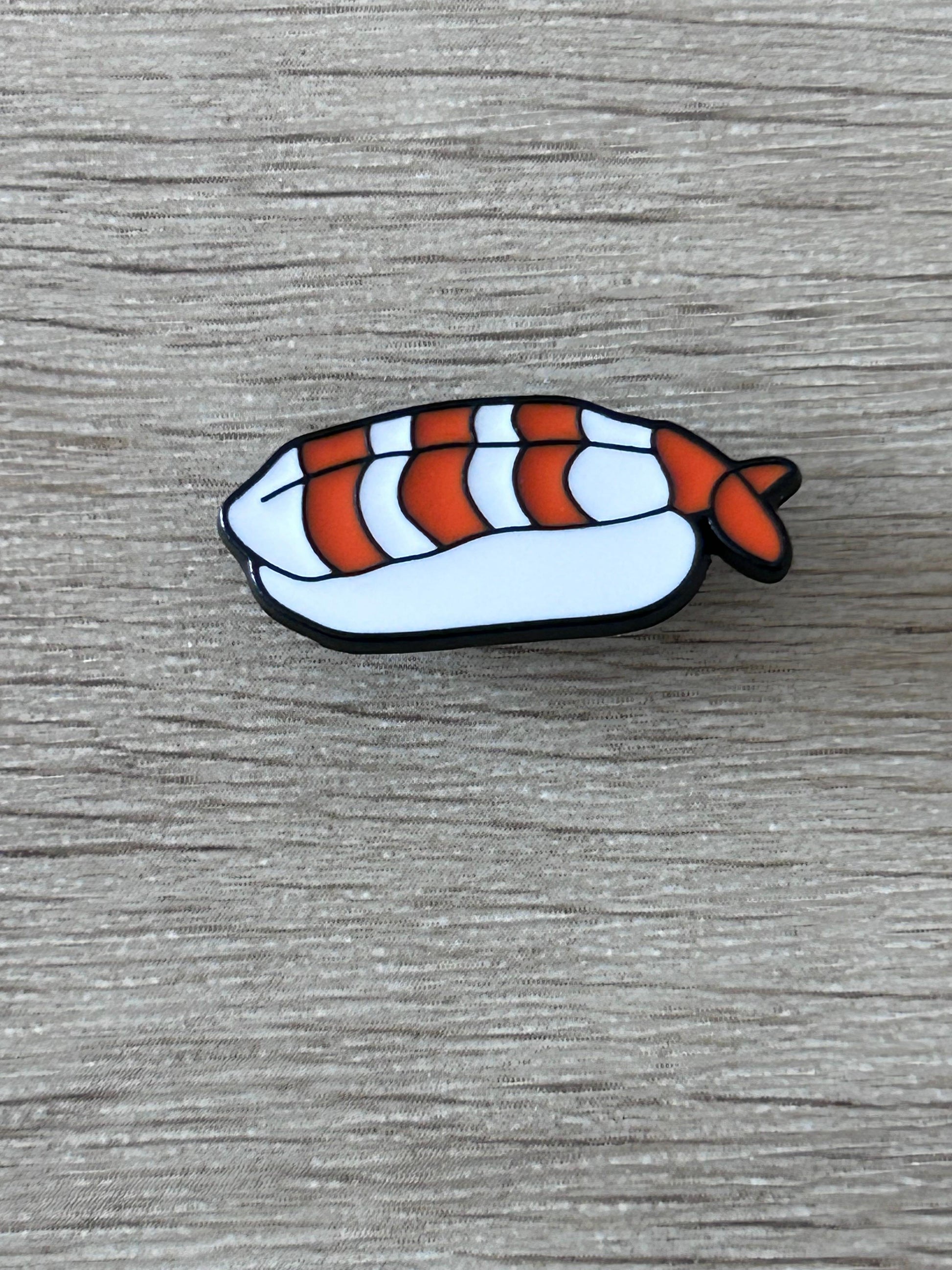 Pin's en forme de nigiri de crevette, blanc, stries bleues, queue orange