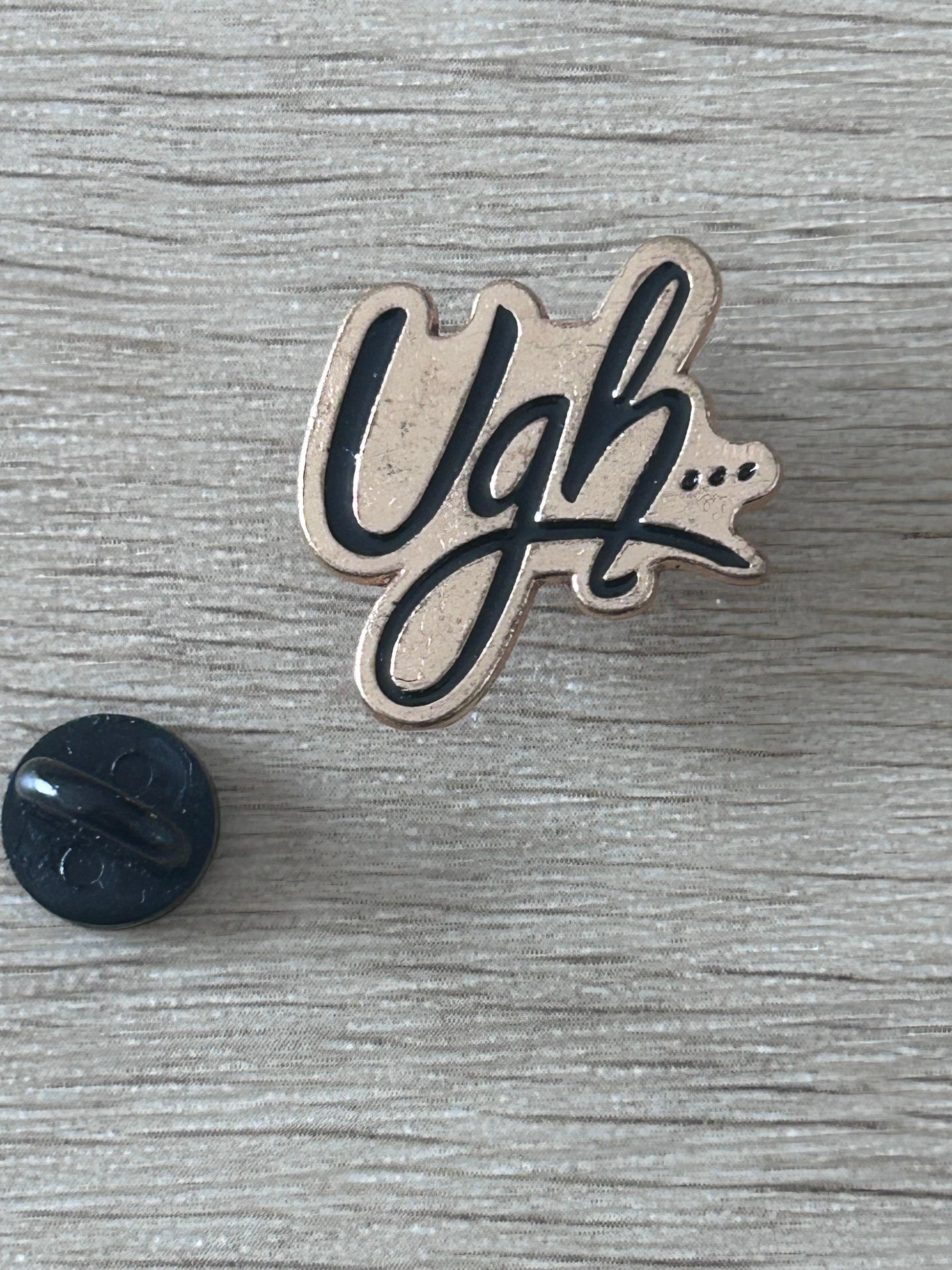 Pin 'Ugh...' émaillé noir et beige avec dos noir.