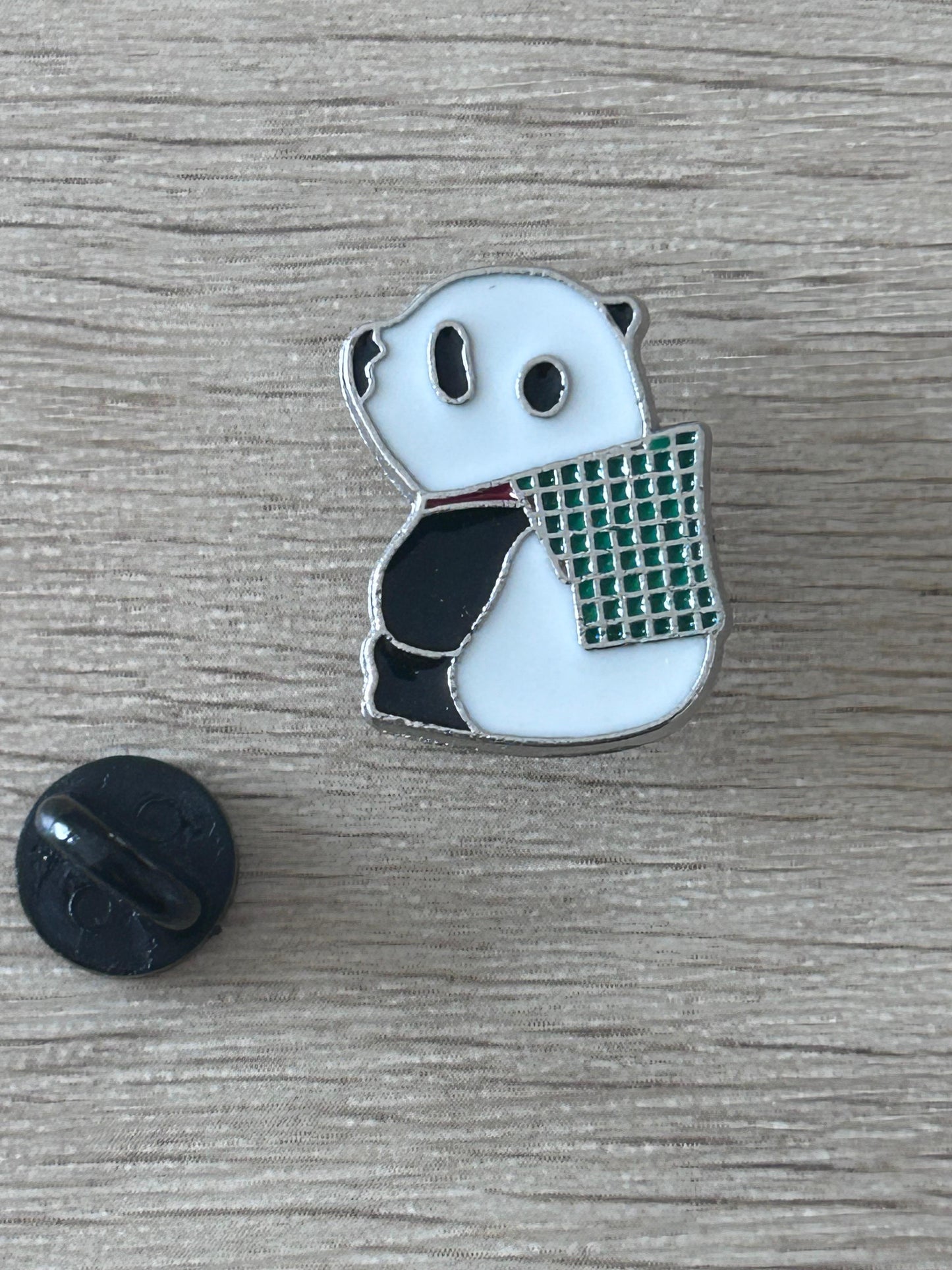 Épingle panda en émail tenant un panier grillagé vert, détails noirs et bleu clair.