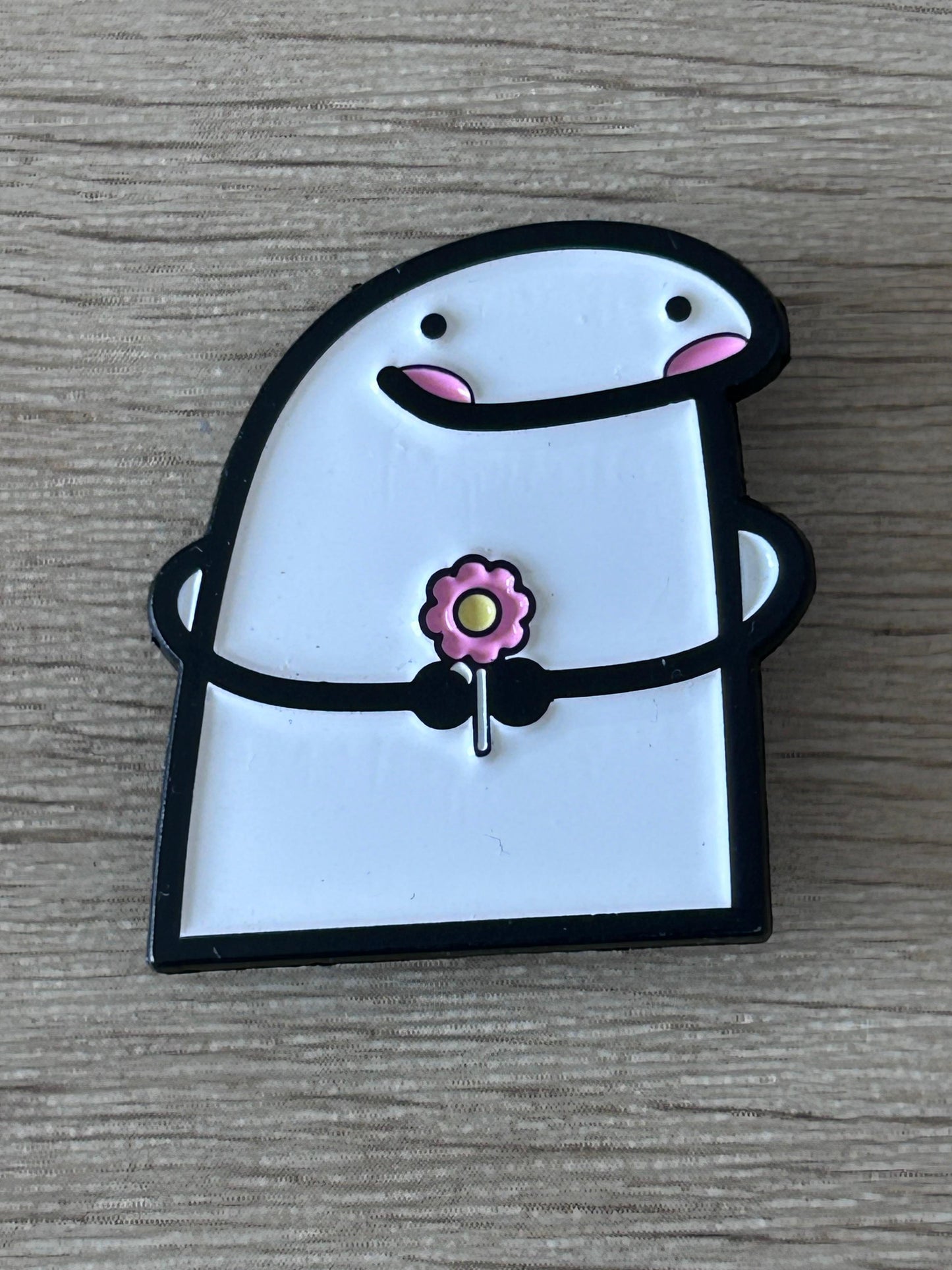 Pin en forme de personnage blanc et noir, fleur rose au centre, yeux et bouche