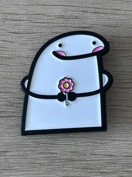 Pin en forme de personnage blanc et noir, fleur rose au centre, yeux et bouche