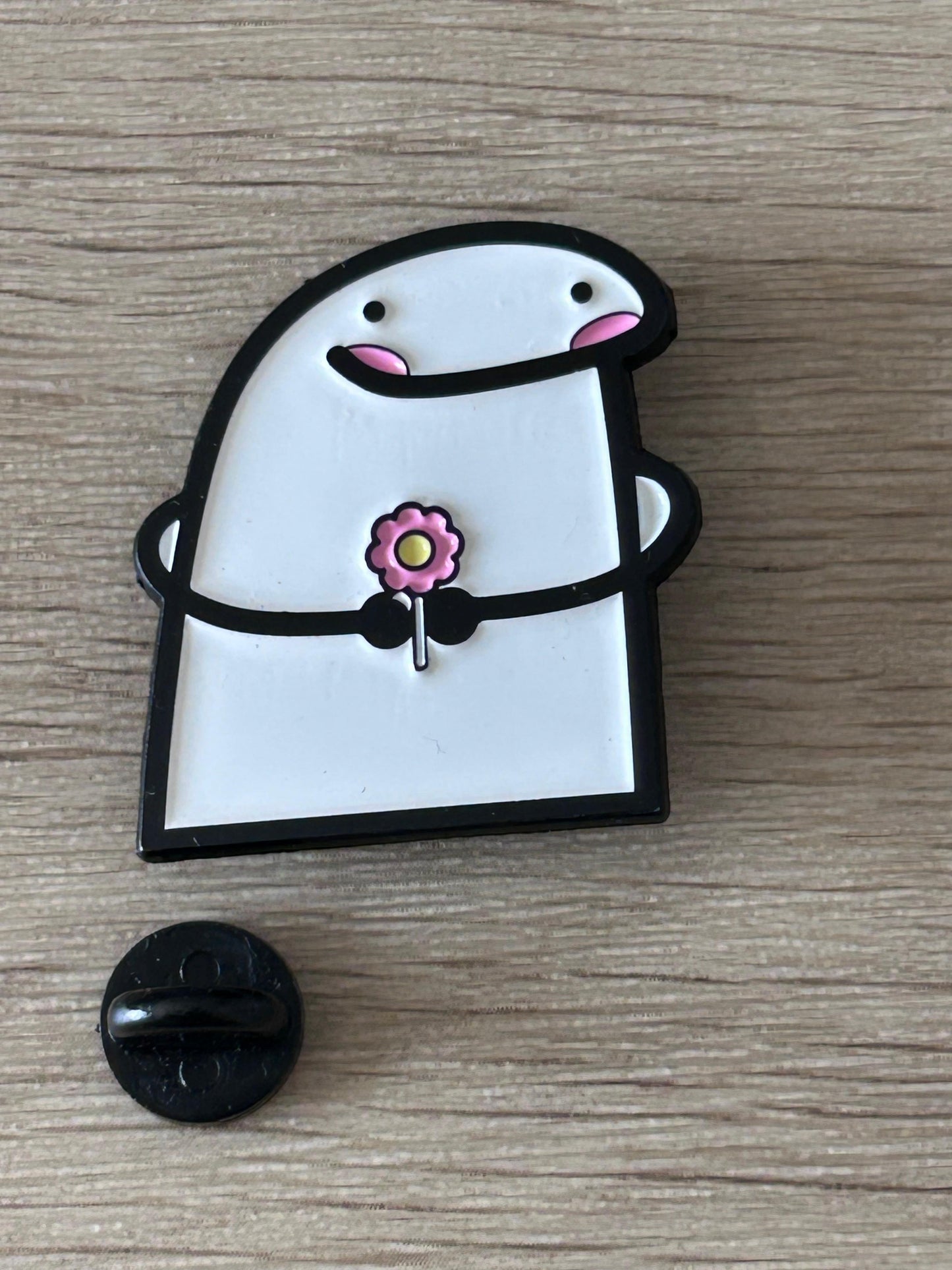 Pin en forme de personnage blanc et noir, fleur rose au centre, dos noir visible