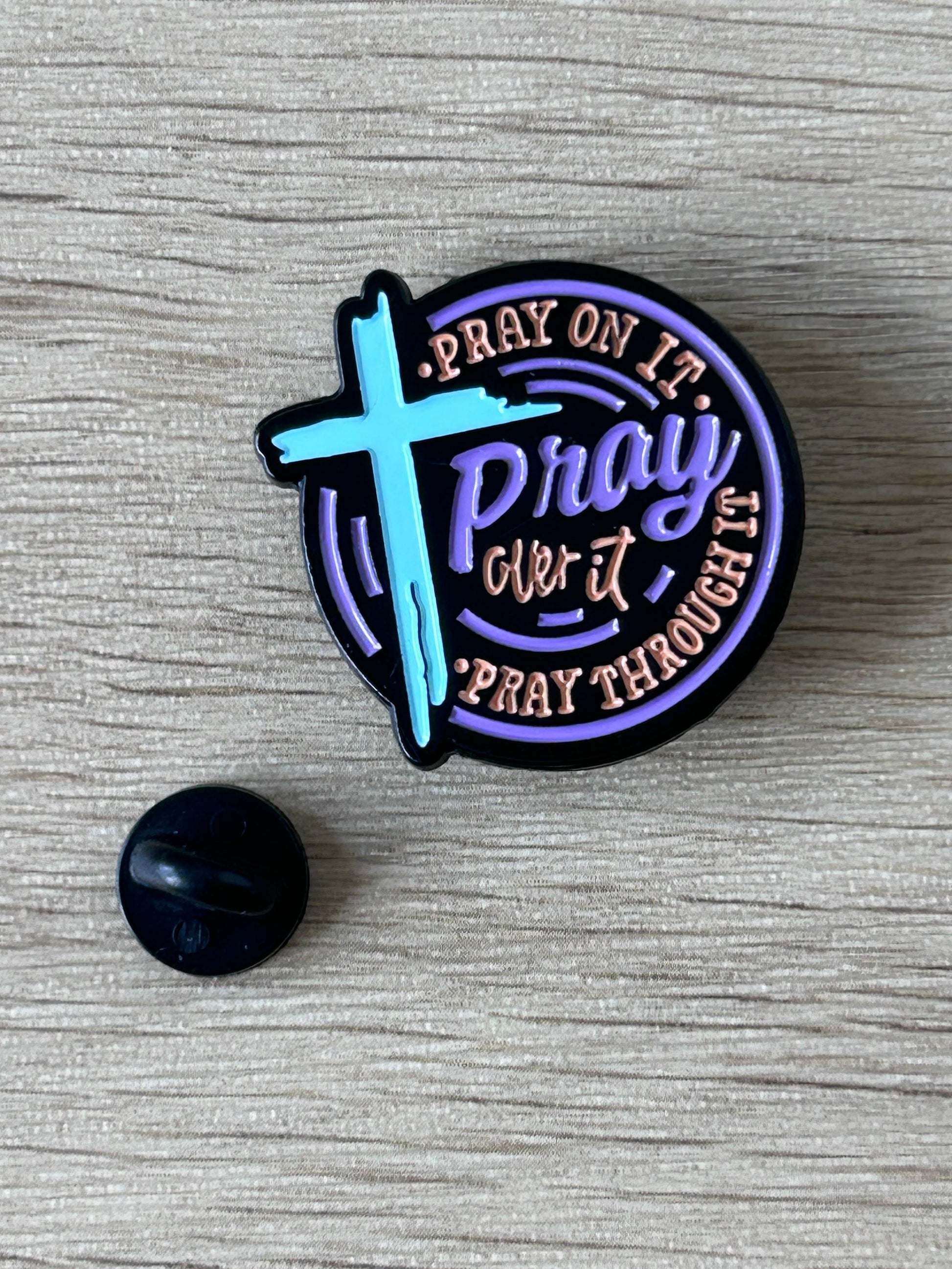 Broche ronde violette et noire avec croix bleue et texte «Pray on it»