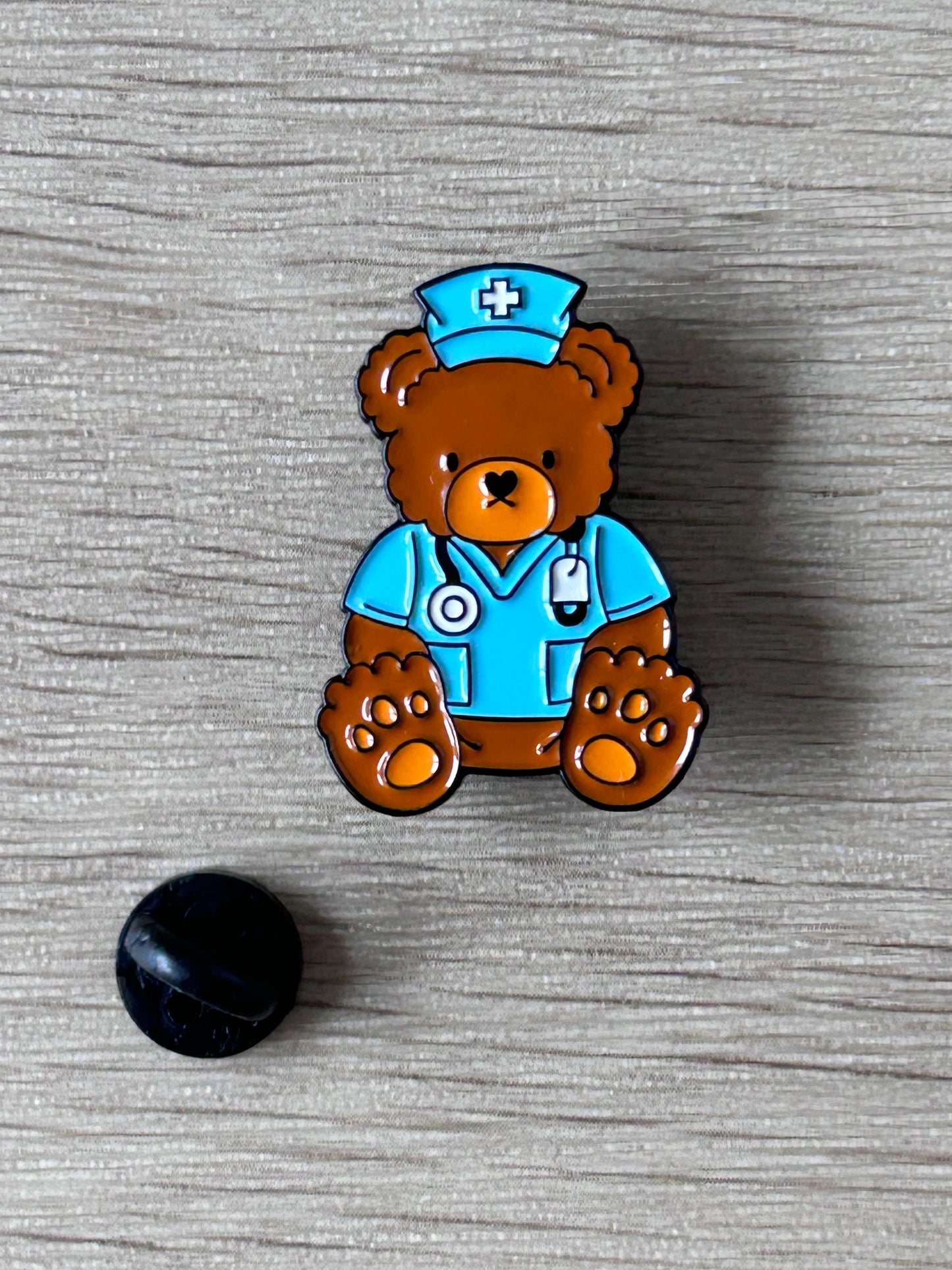 Épinglette ourson docteur brun et bleu avec croix blanche et stéthoscope, plus pastille noire