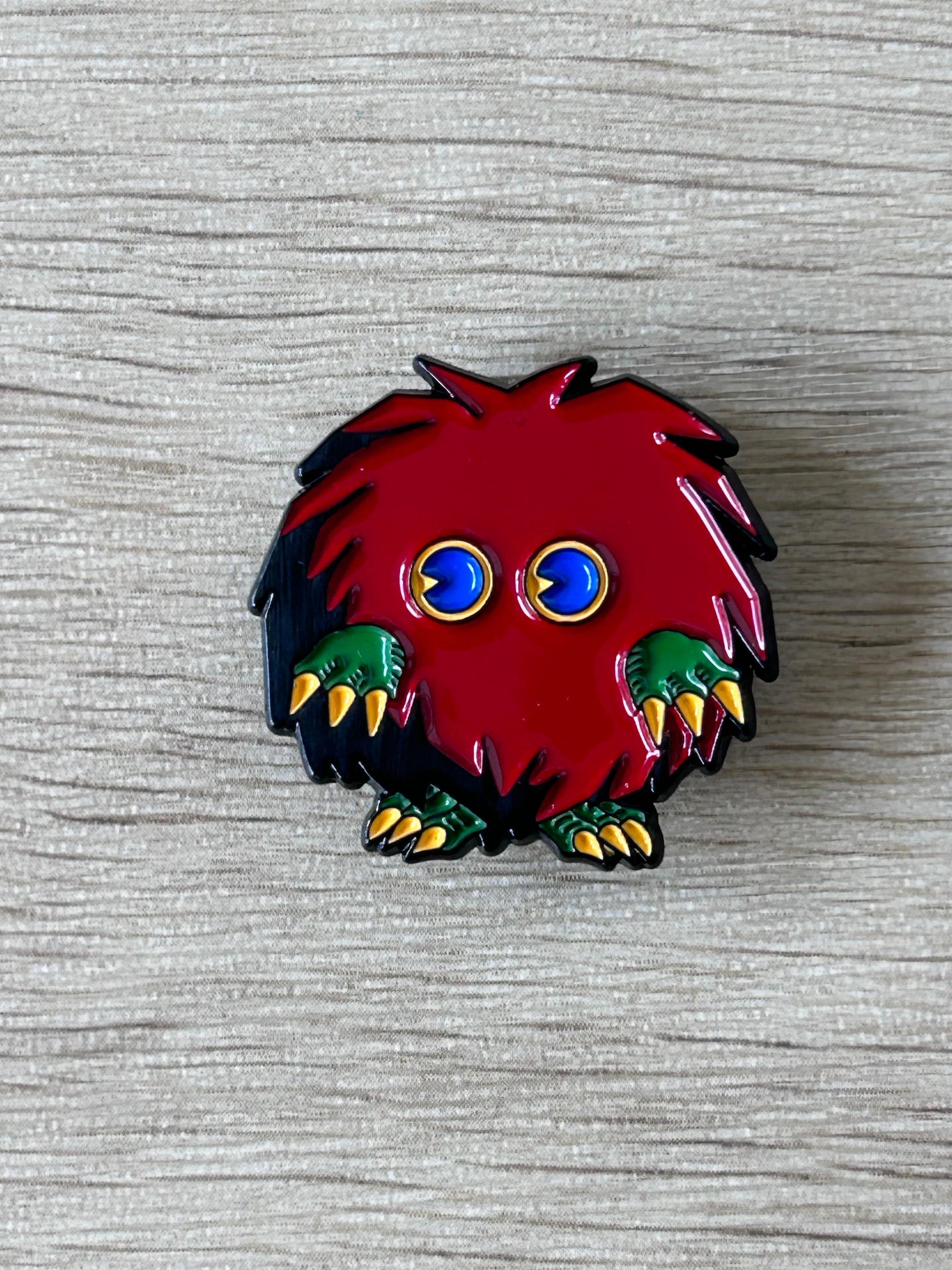 Pin's de monstre rouge poilu, yeux bleus et griffes vertes.
