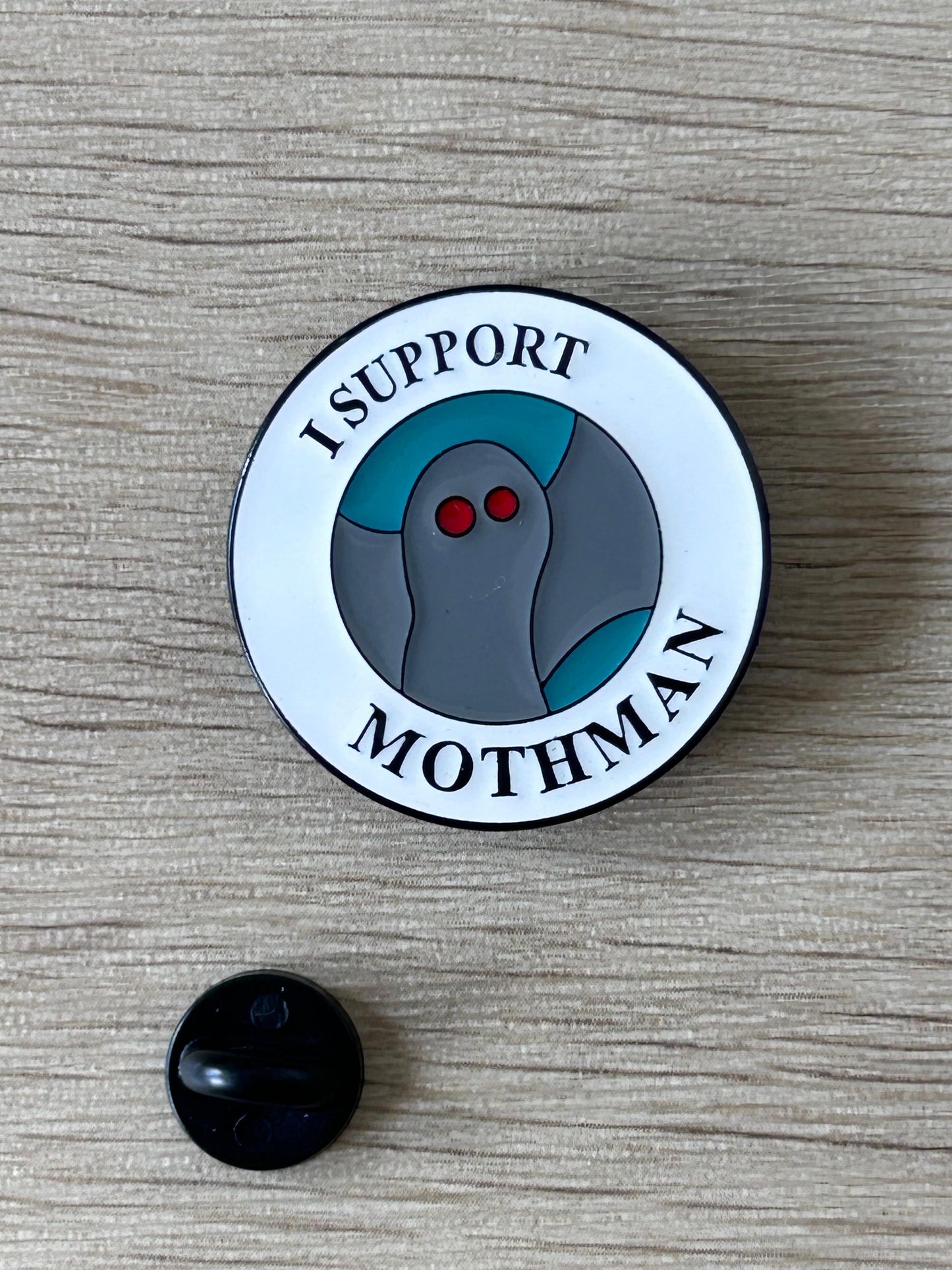 Badge rond I SUPPORT MOTHMAN avec motif mothman gris, yeux rouges; dos noir visible