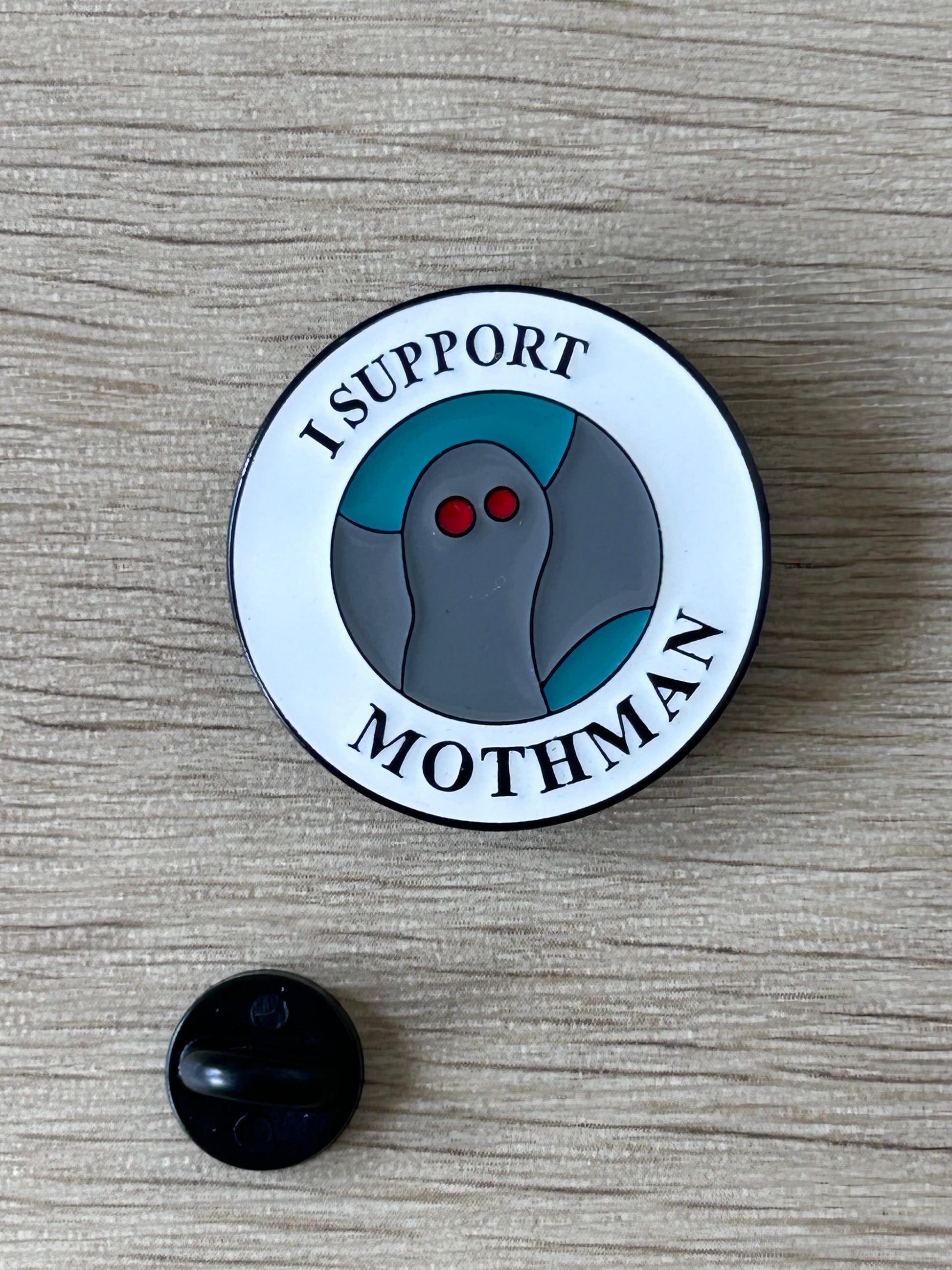 Badge rond I SUPPORT MOTHMAN avec motif mothman gris, yeux rouges; dos noir visible