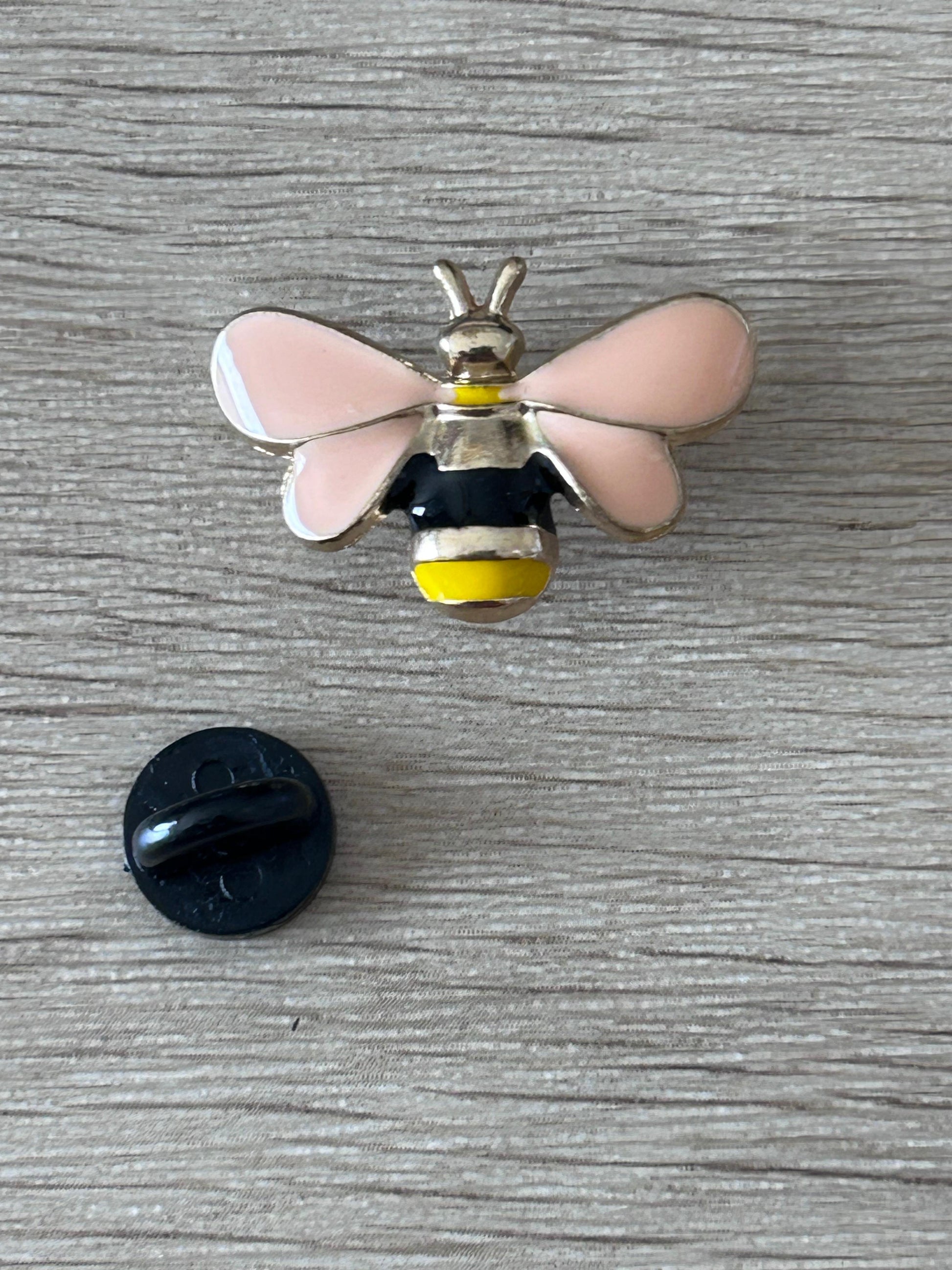 Pin's abeille en relief: ailes roses, corps noir et jaune, avec attache arrière noire.