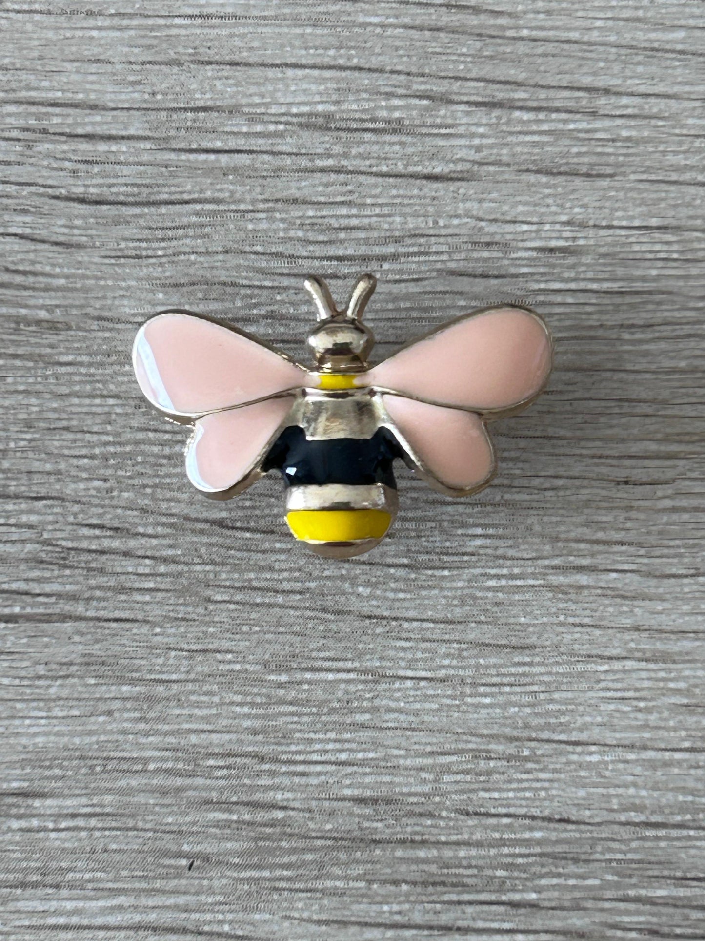Pin's abeille en relief: ailes roses, corps noir et jaune, antennes dorées.