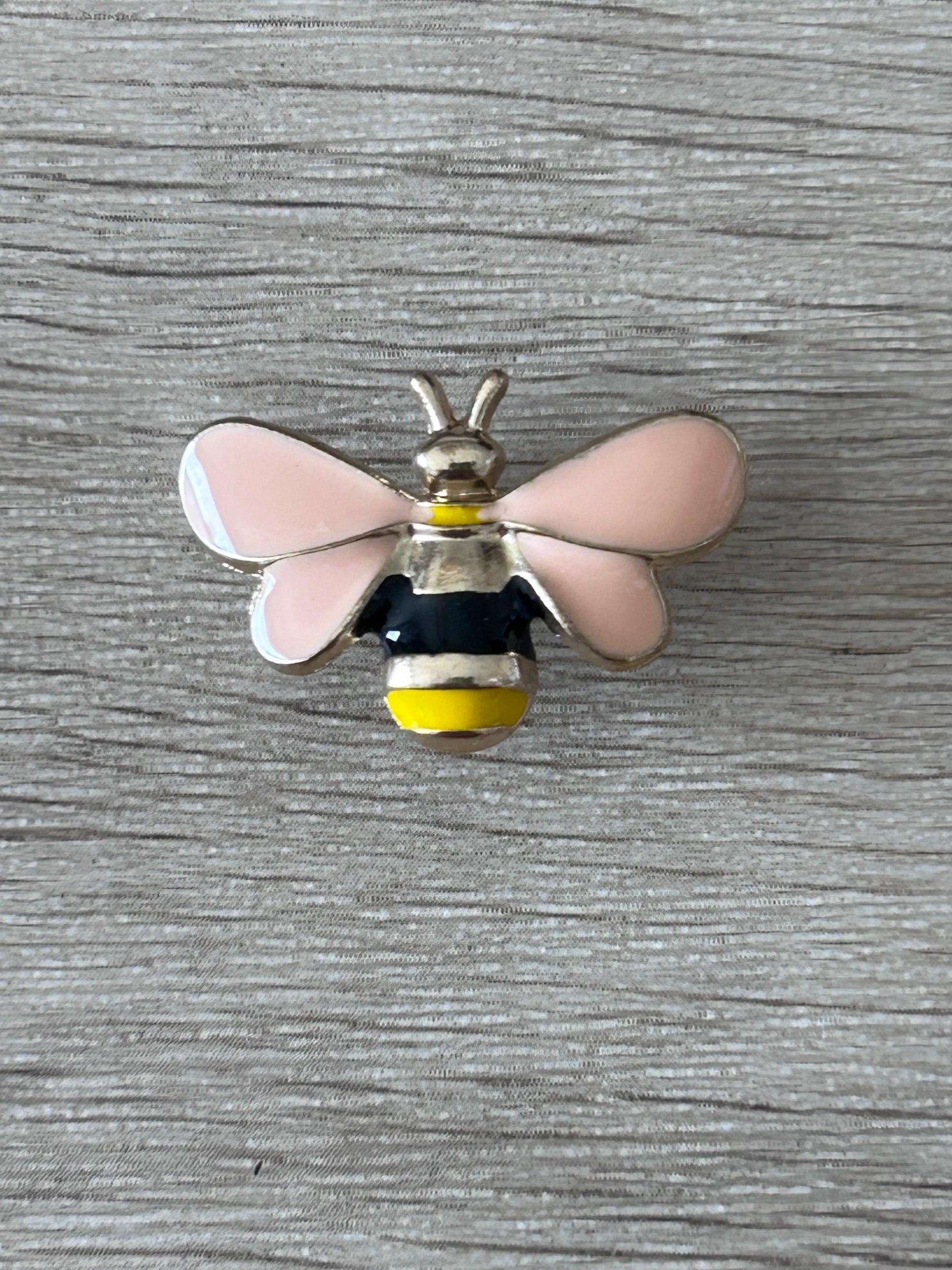 Pin's abeille en relief: ailes roses, corps noir et jaune, antennes dorées.