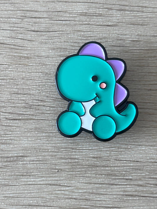 Broche dinosaure bébé kawaii turquoise et violet, contour noir, tête souriante.
