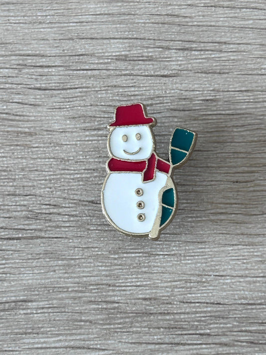Broche bonhomme de neige émaillée : chapeau rouge, écharpe verte, bonhomme blanc souriant.