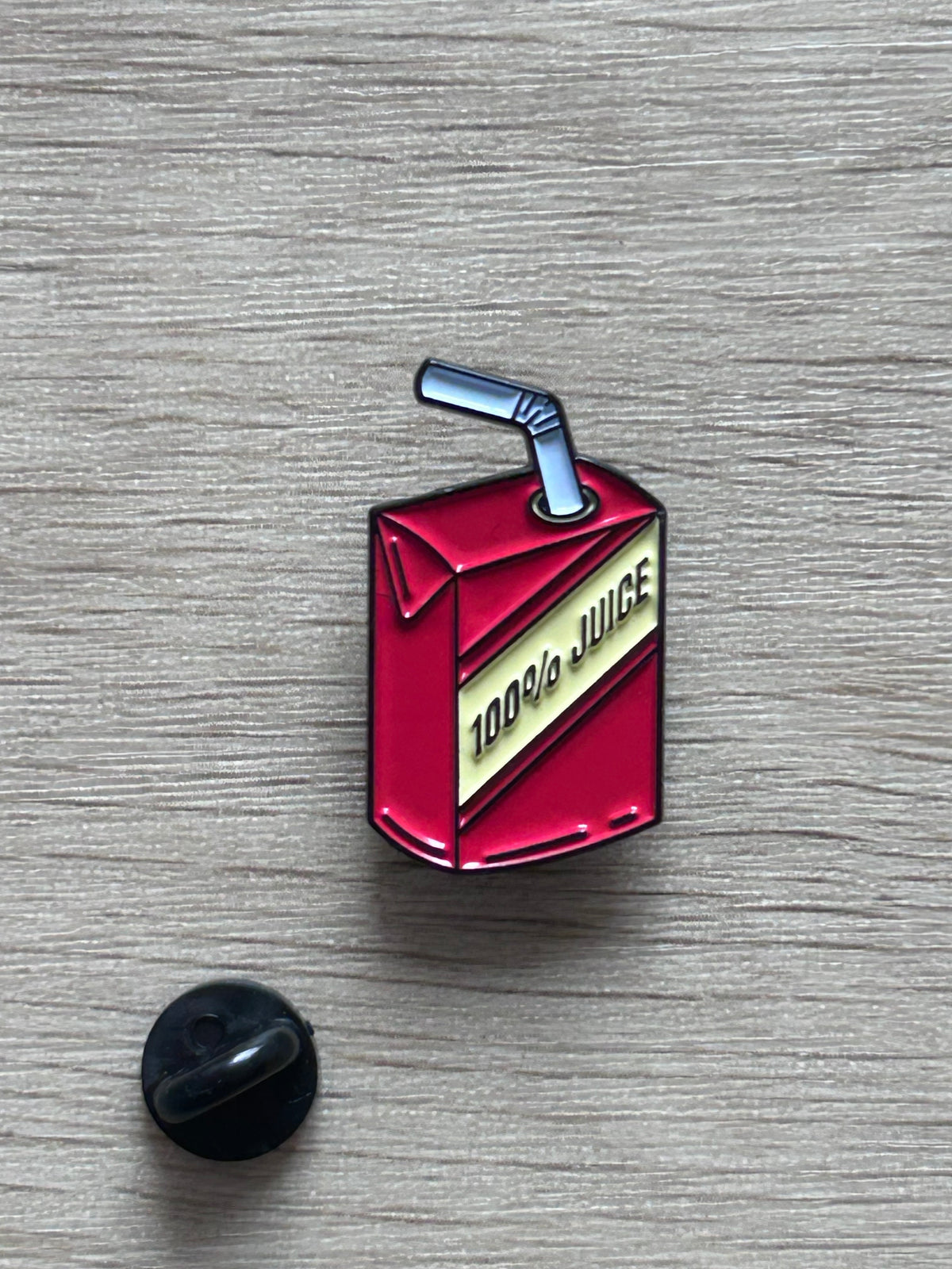 Détail d’un pin's brique de jus rouge et jaune avec paille bleue