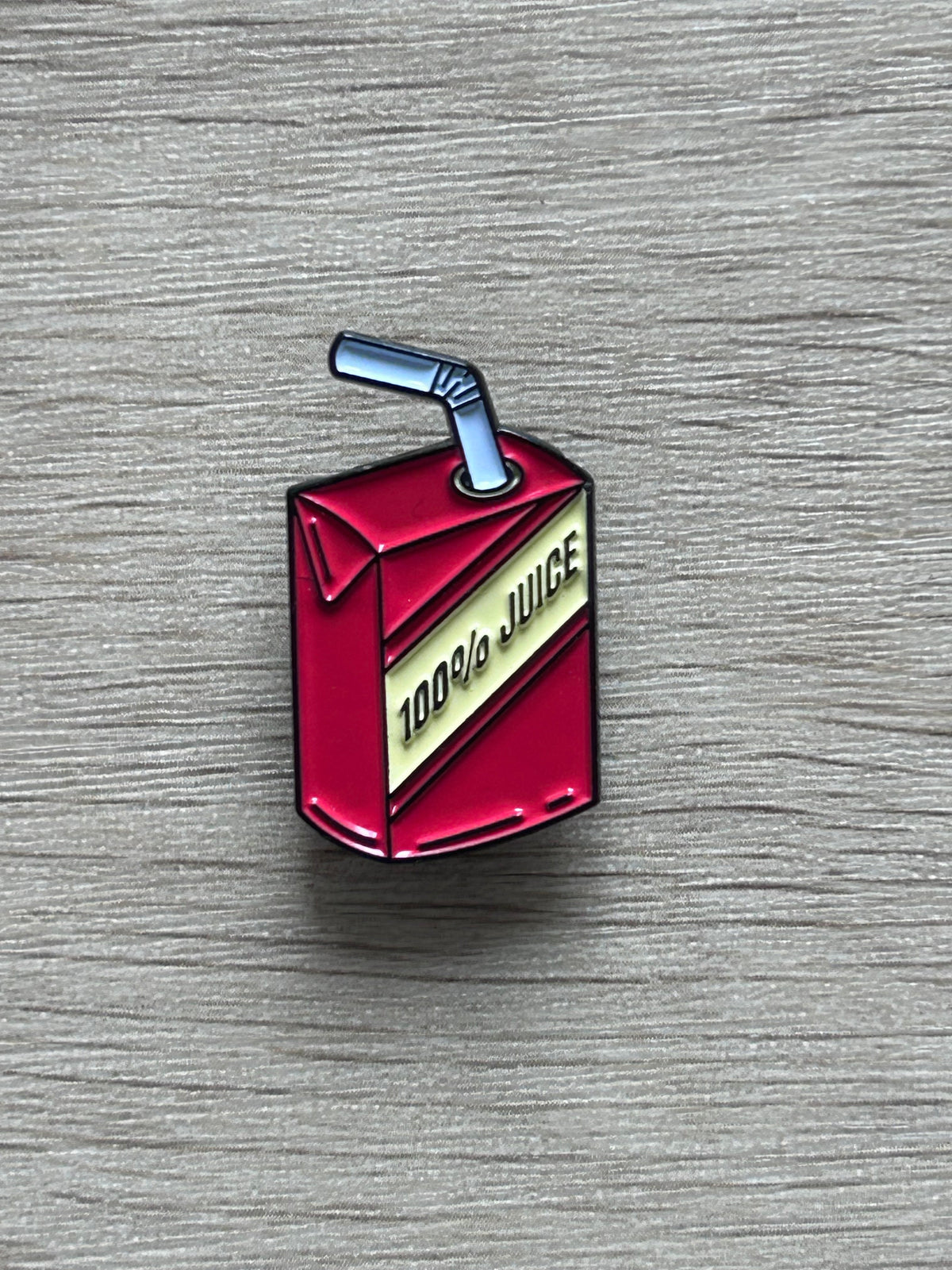 Pin's représentant une brique de jus rouge avec une paille bleue
