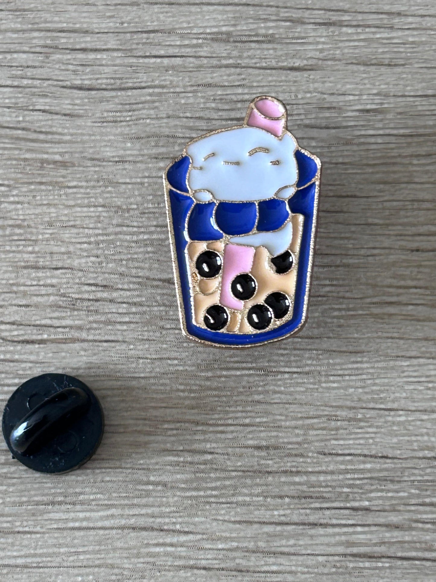 Broche gobelet bubble tea bleu kawaii, visage, et disque noir visible au premier plan