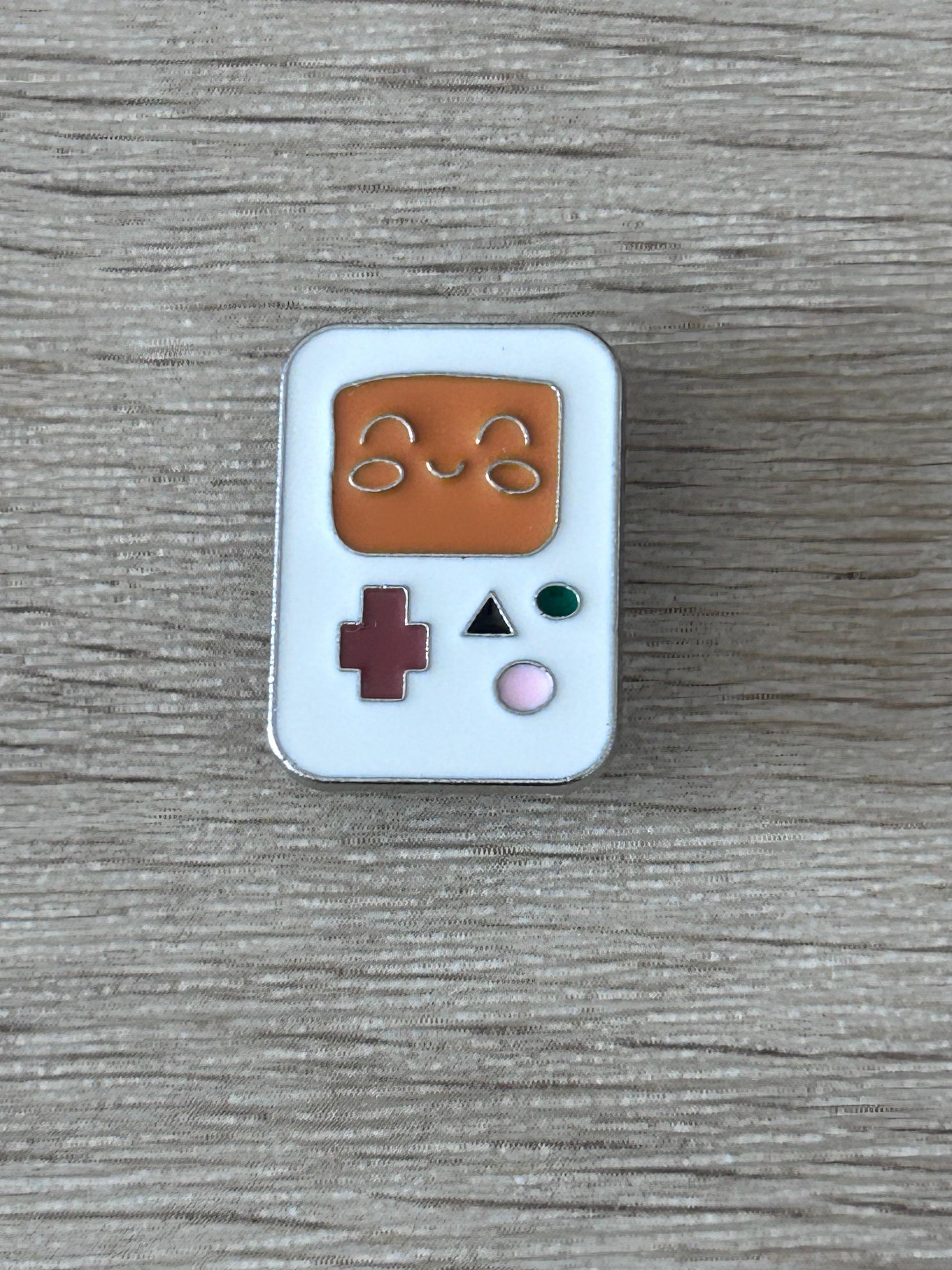 Pin’s console portable kawaii émail bleu clair, manette brune avec bouton +, vert et rose.