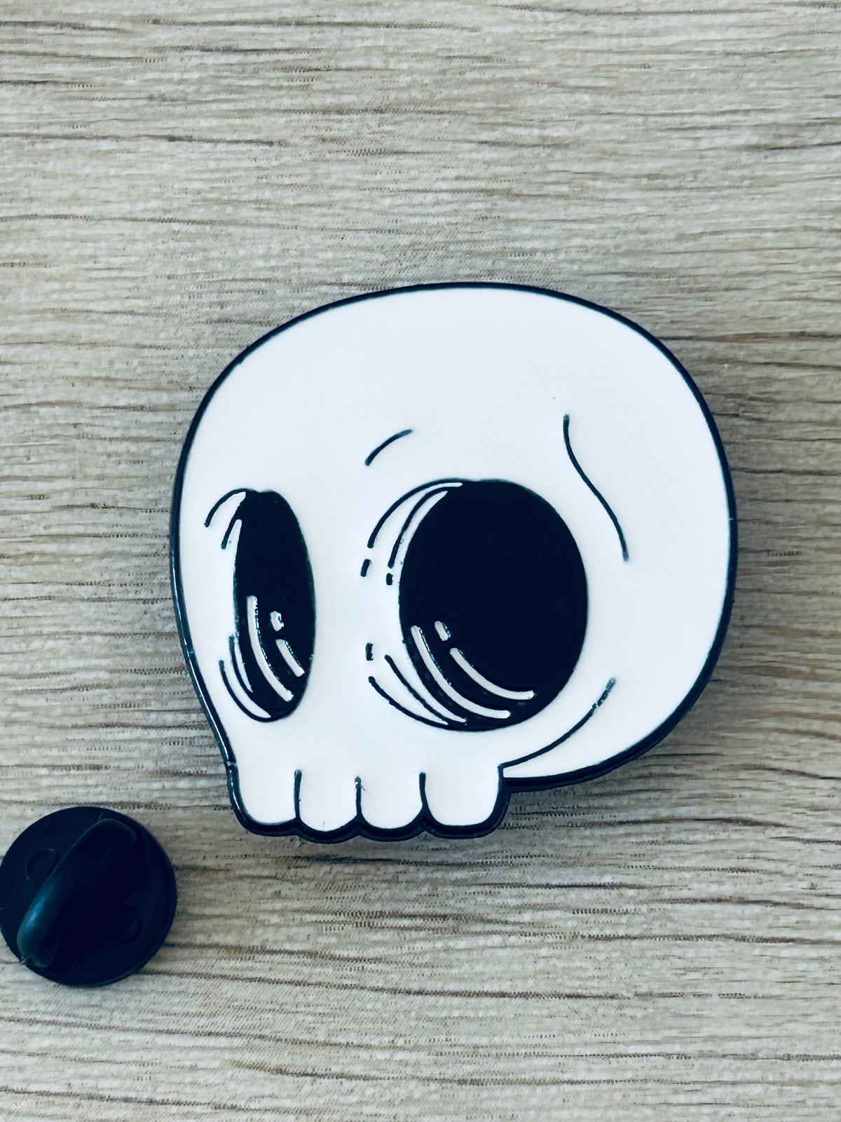 Pin tête de mort kawaii blanc avec contour noir, gros yeux stylisés