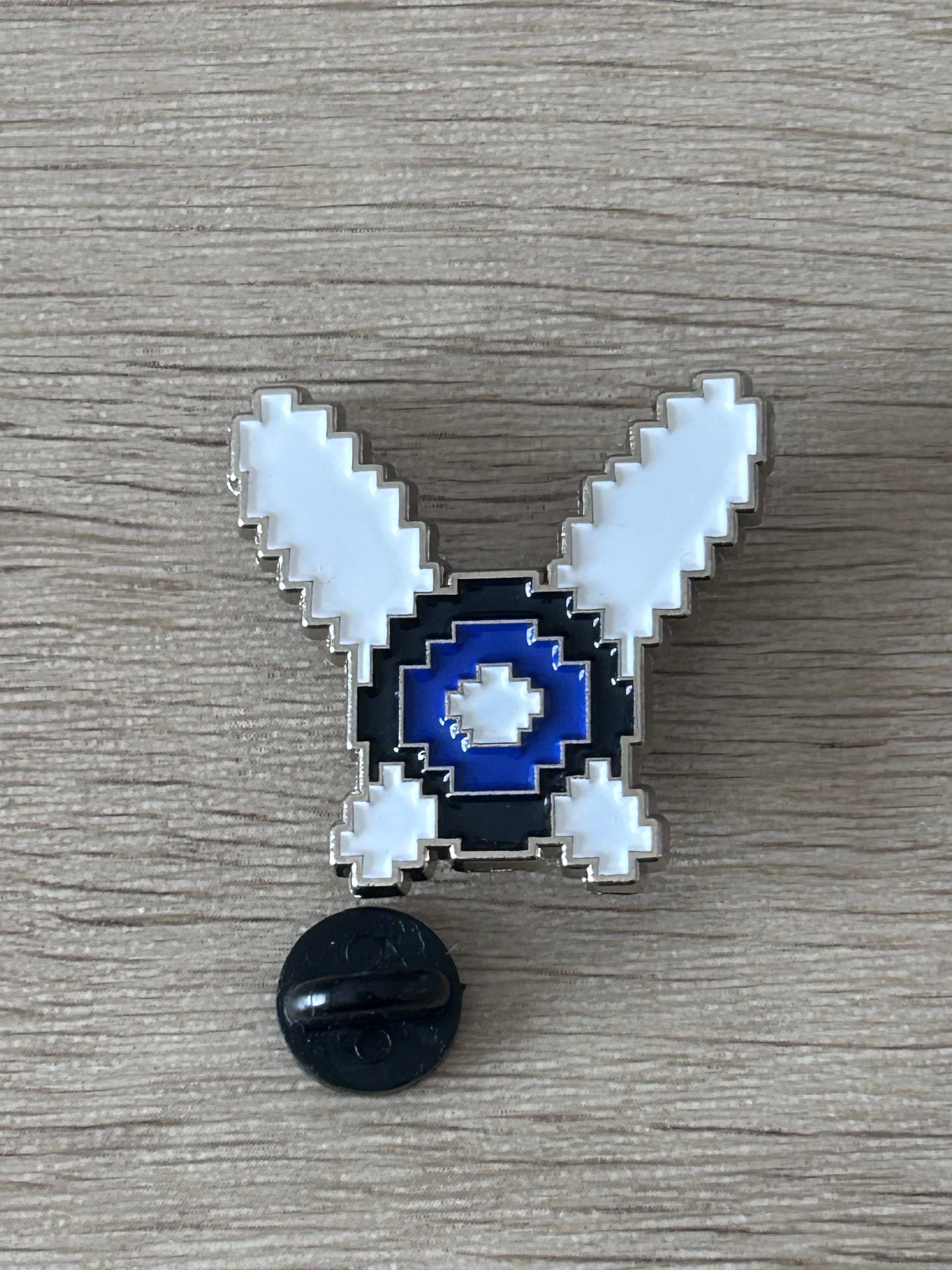 Broche fée pixel art bleu marine et bleu clair, ailes en V, dos noir visible.