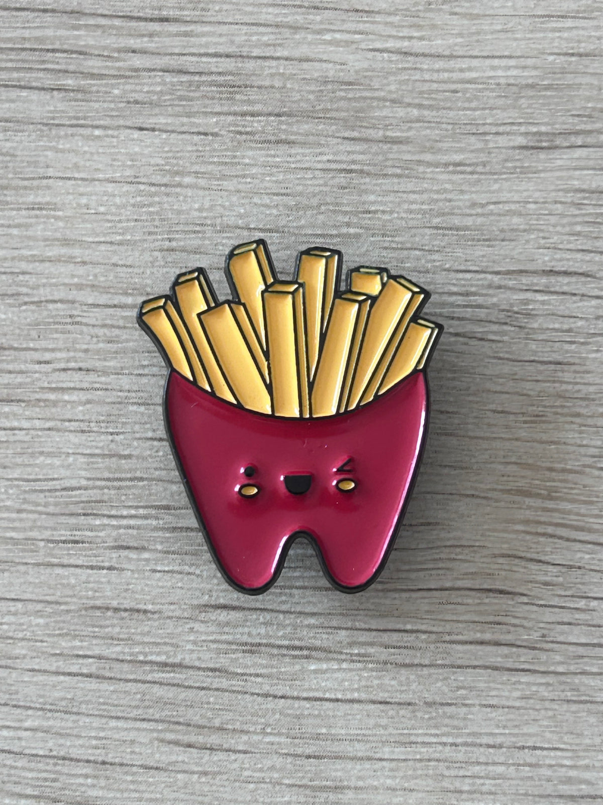 Détail d’un pin's frites souriantes en émail jaune et rouge