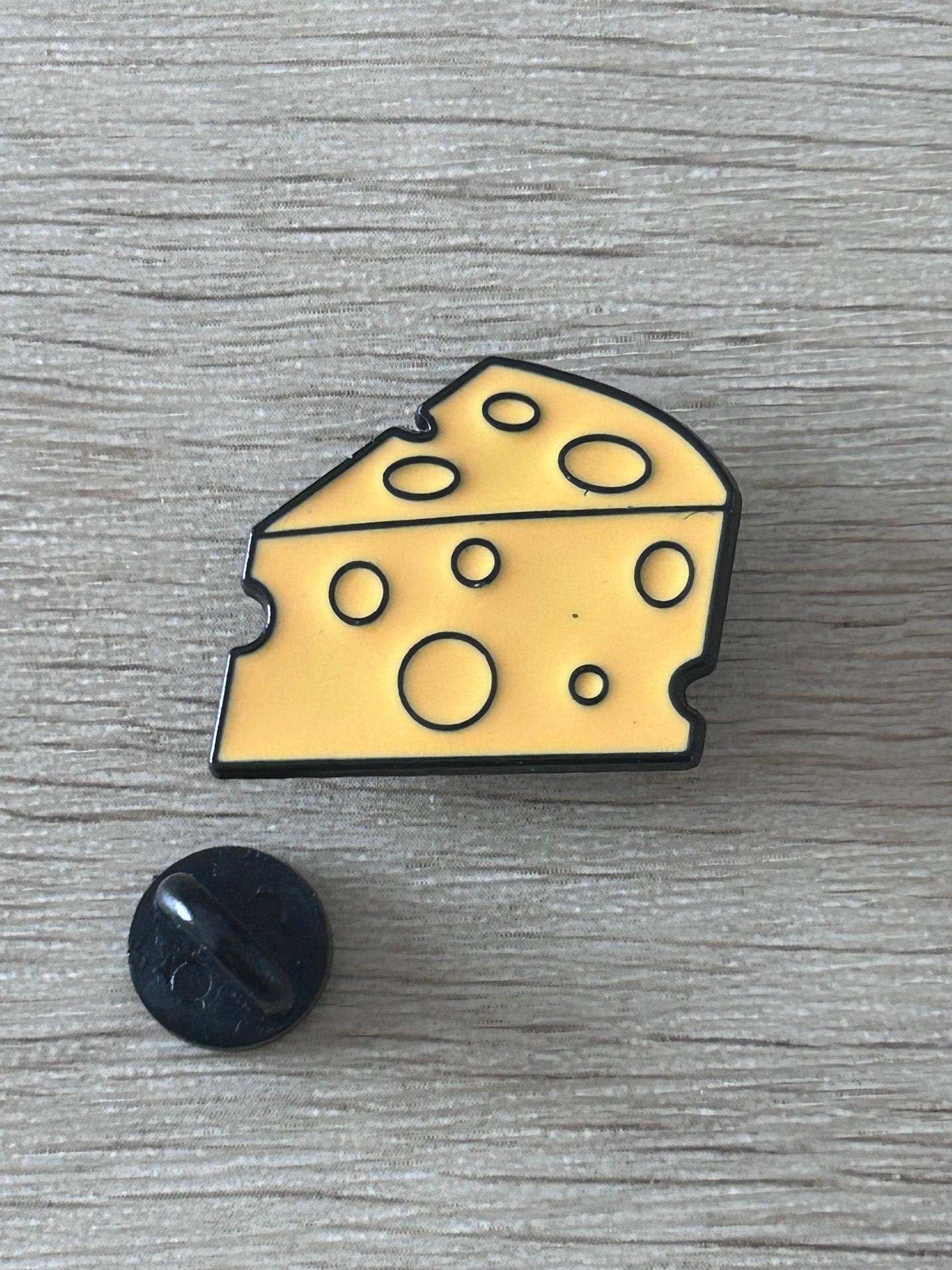 Pin's fromage jaune à trous, avec attache noire au revers visible.