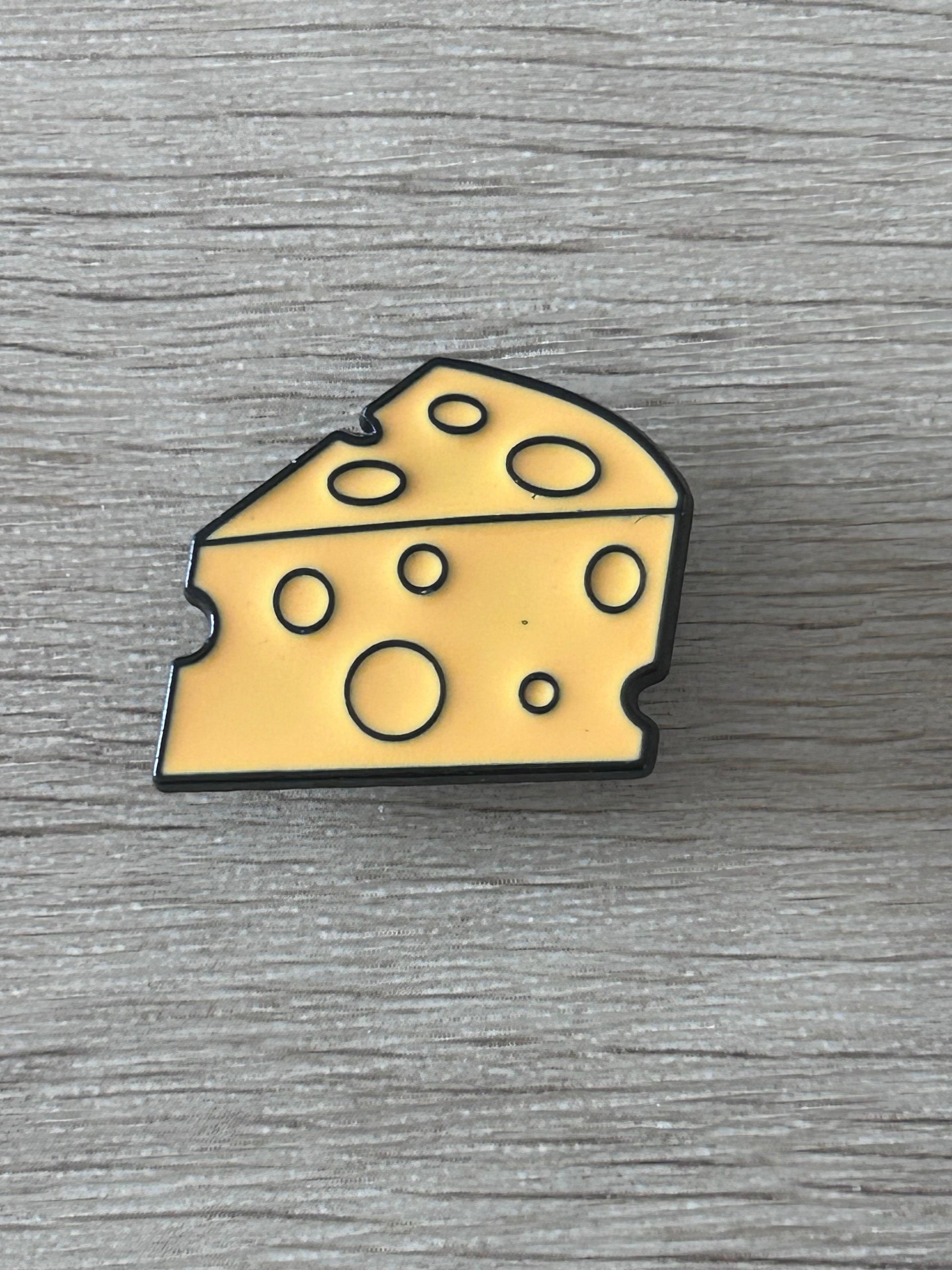Pin's fromage en forme de tranche de fromage jaune, contours noirs, motifs de trous.