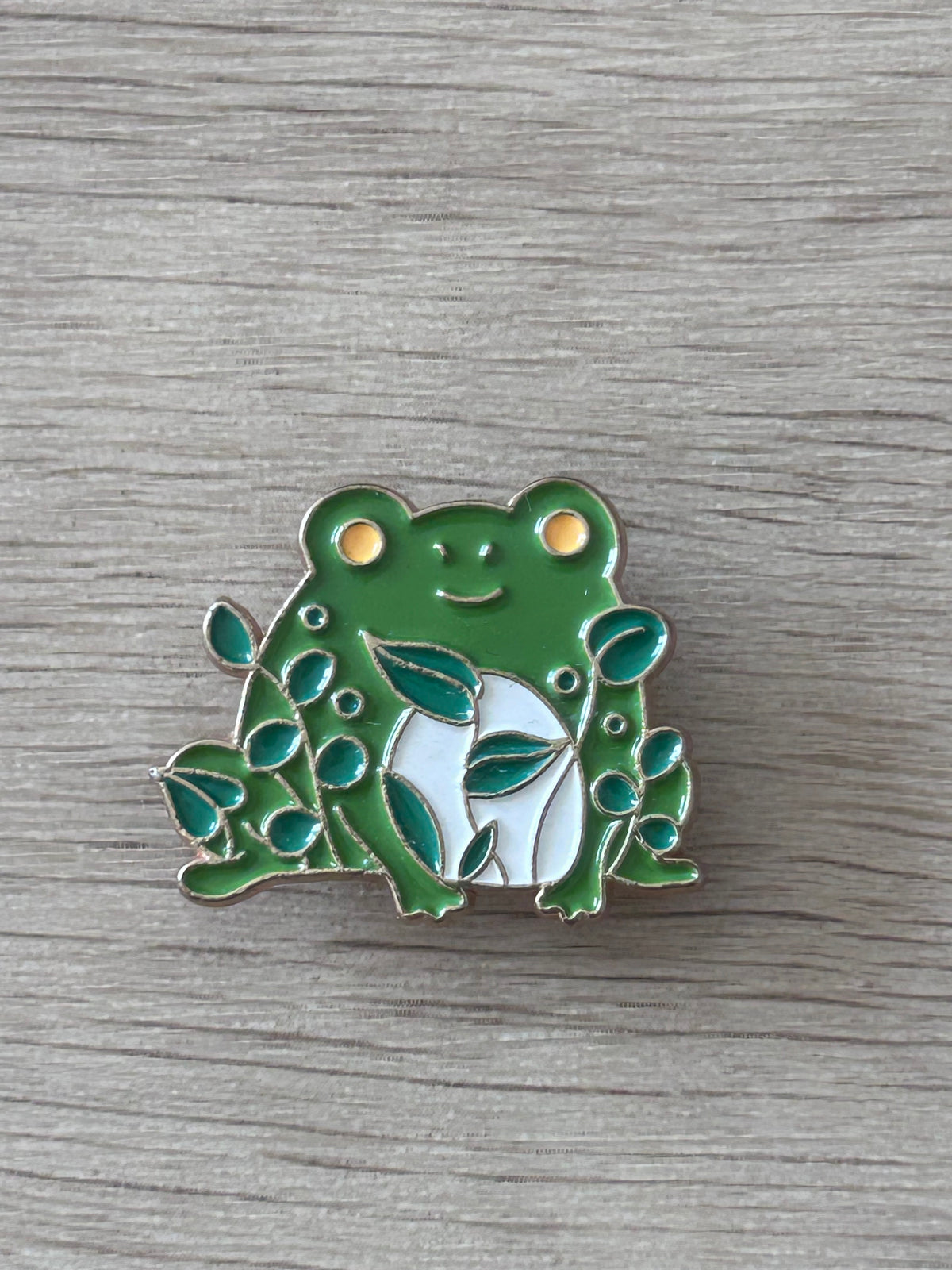 Pin émaillé grenouille verte avec feuillage, yeux dorés