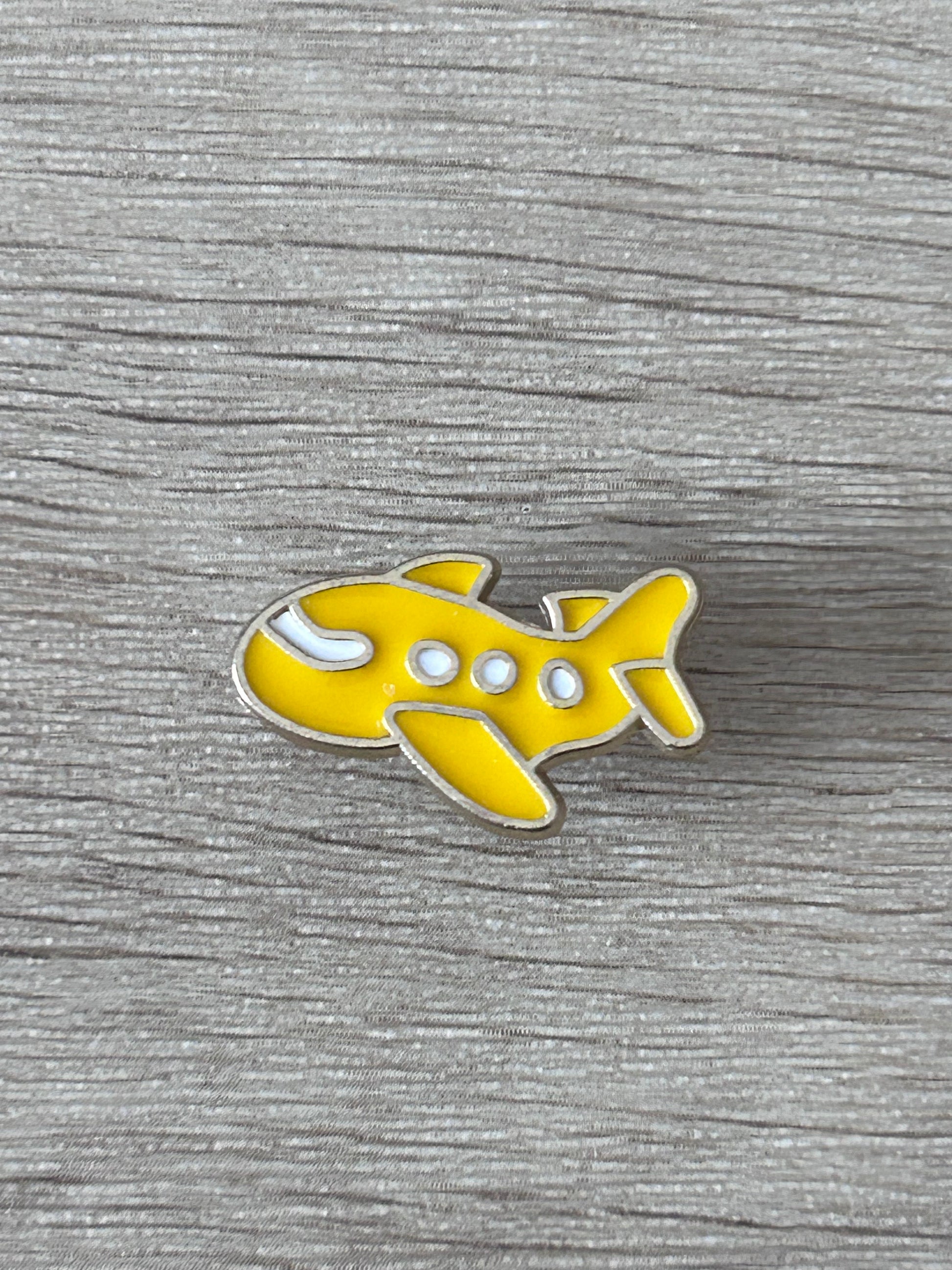 Broche avion jaune kawaii en métal, vue rapprochée, émail blanc.