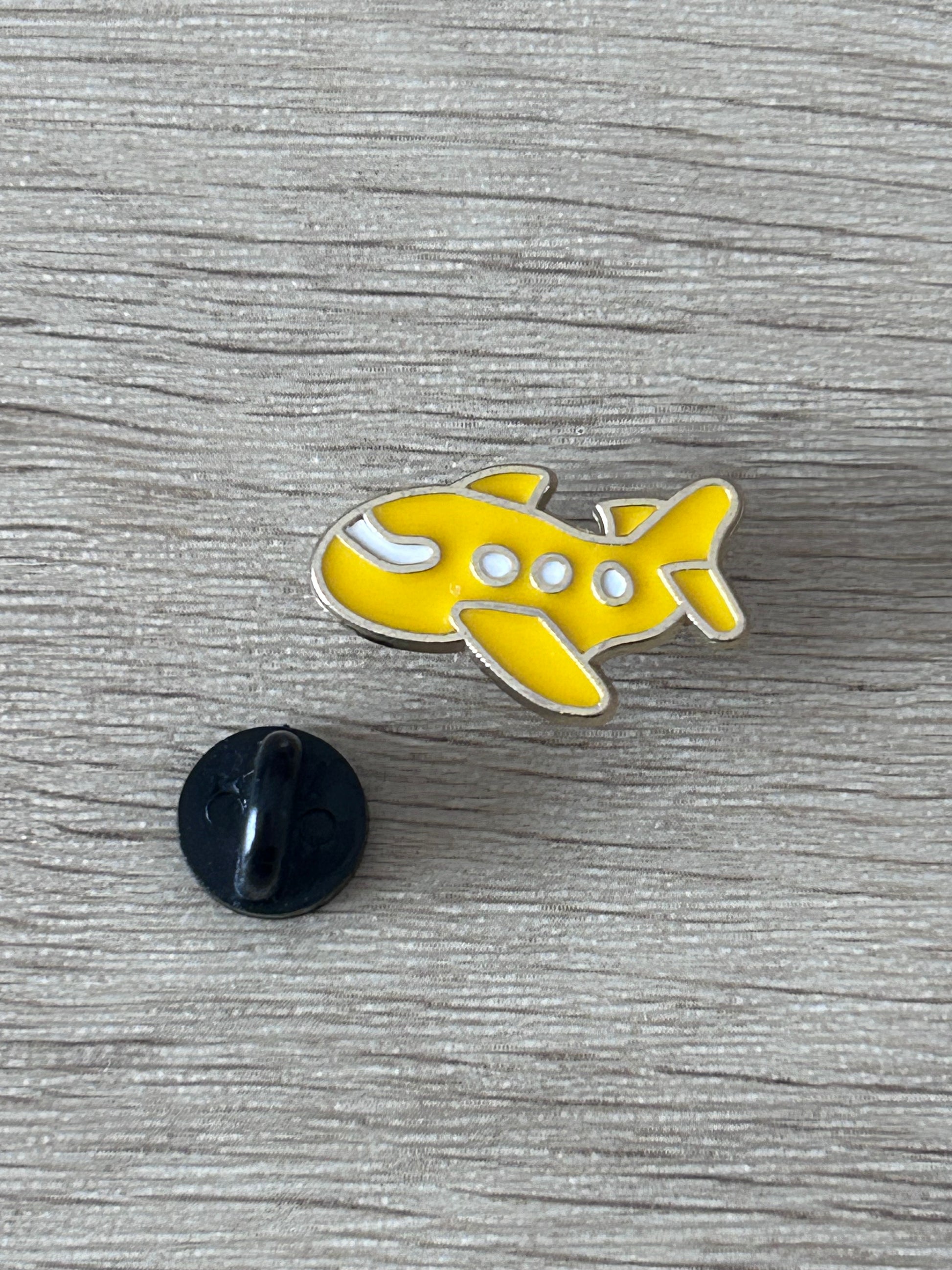 Broche avion jaune kawaii en métal, attache noire et détails blancs.
