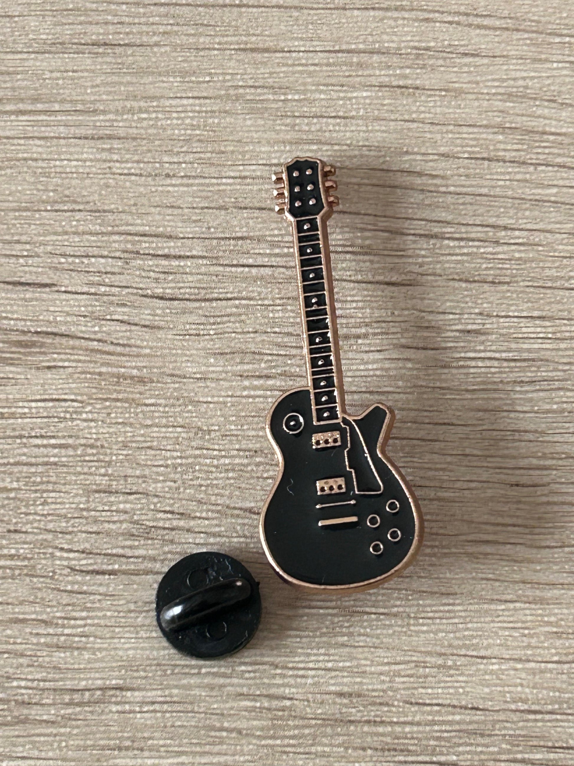 Broche guitare électrique noire avec fermeture noire, cordes et boutons visibles.