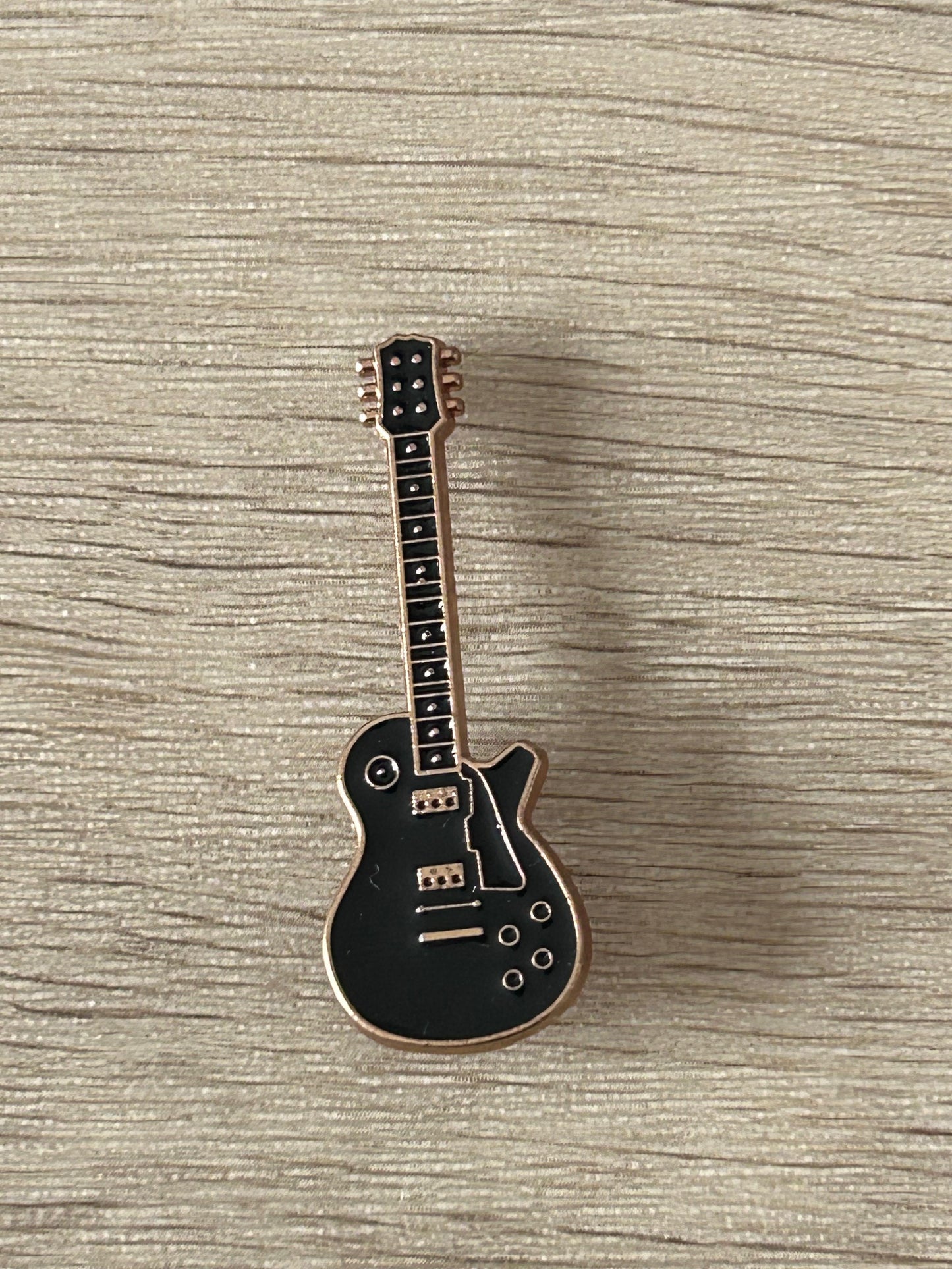 Broche en forme de guitare électrique noire, silhouette détaillée et cordes visibles.