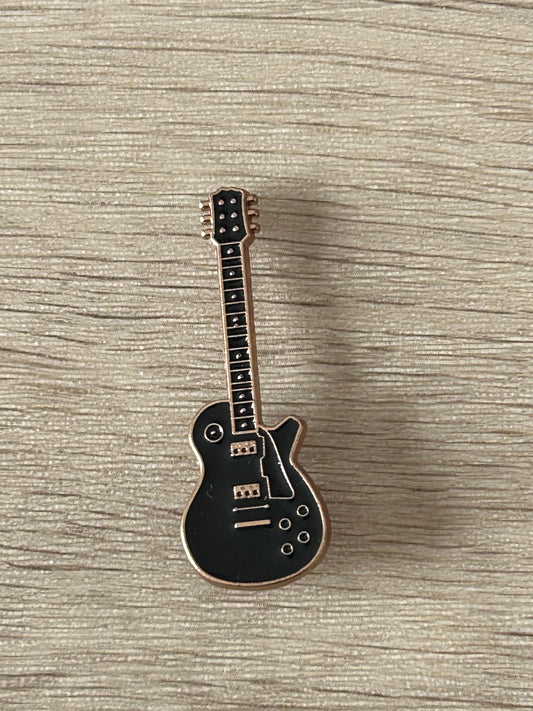 Broche en forme de guitare électrique noire, silhouette détaillée et cordes visibles.