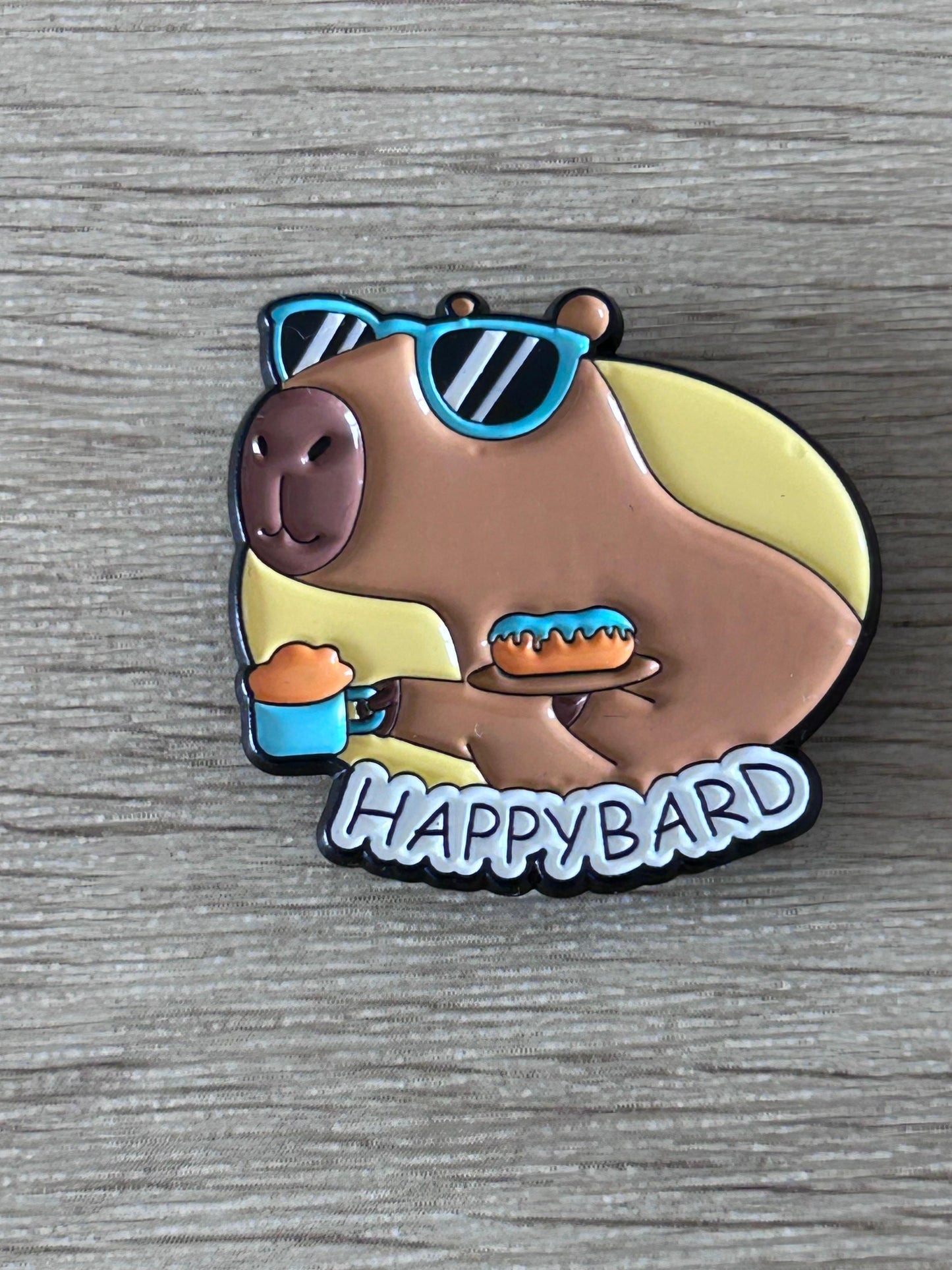 Pin capybara «Happybard» émaillé marron, lunettes bleues et boisson orange.