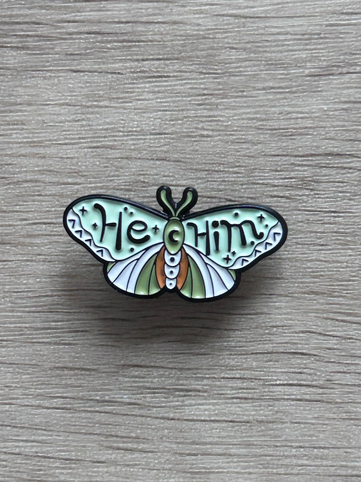 Pin's he/him coloré avec personnage vert sur fond en bois