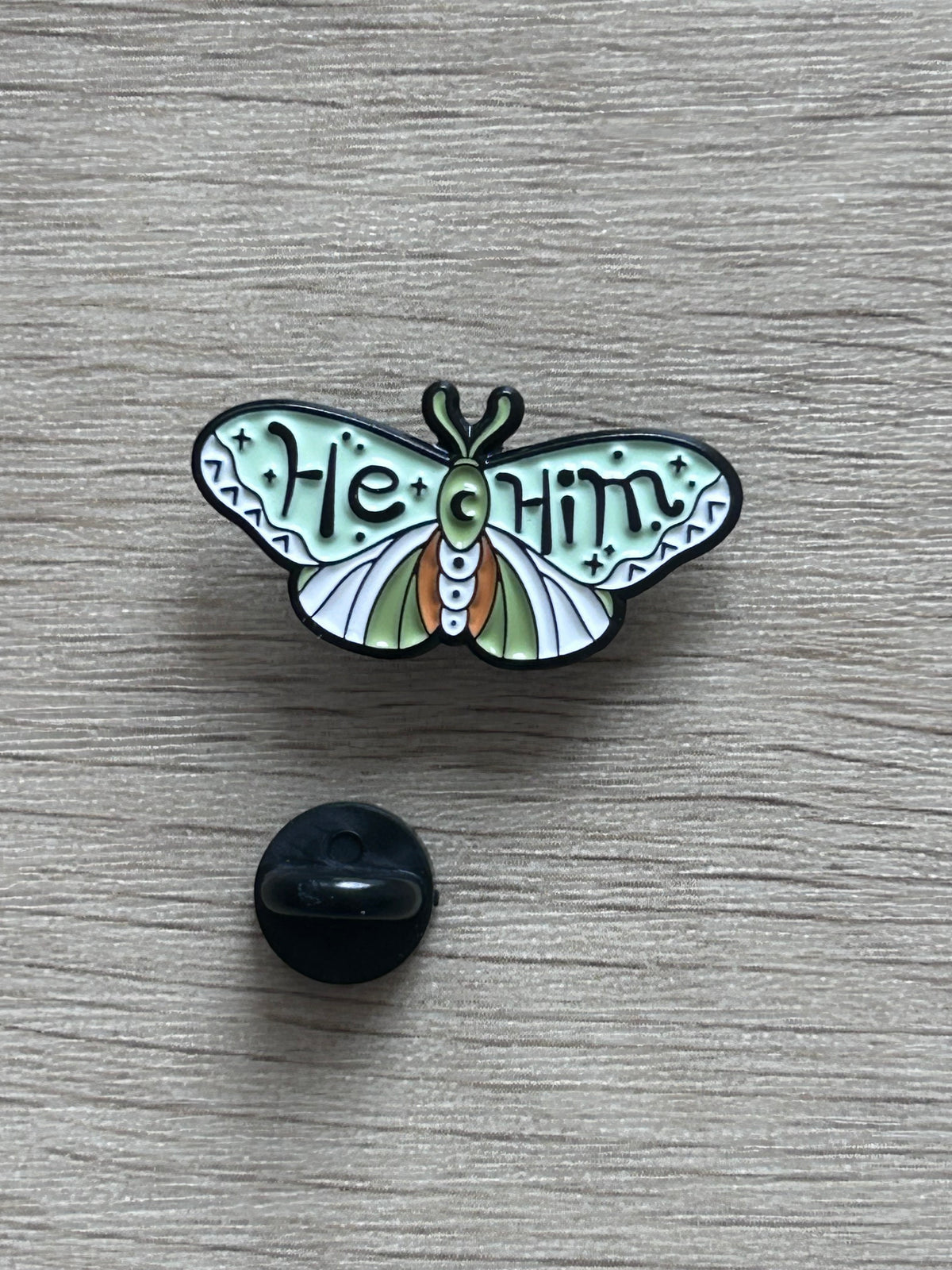 Détail du pin's he/him avec inscription colorée