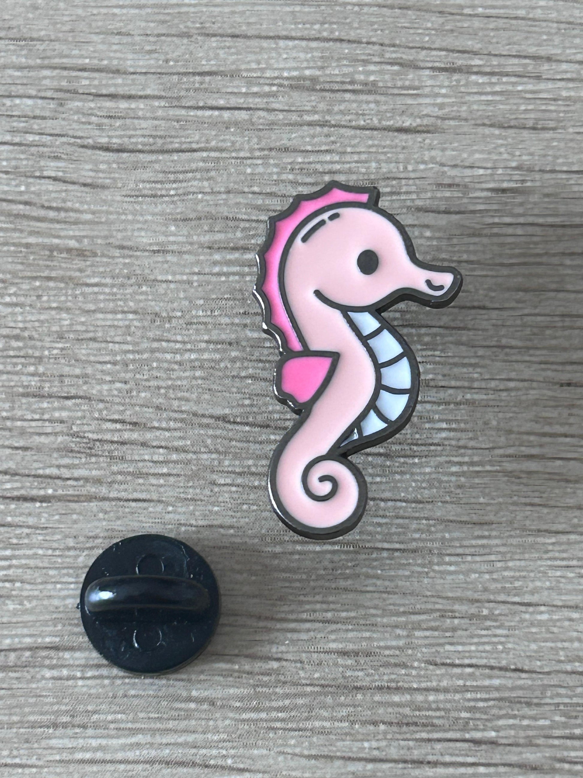 Pin hippocampe rose avec dos noir et patte levée.