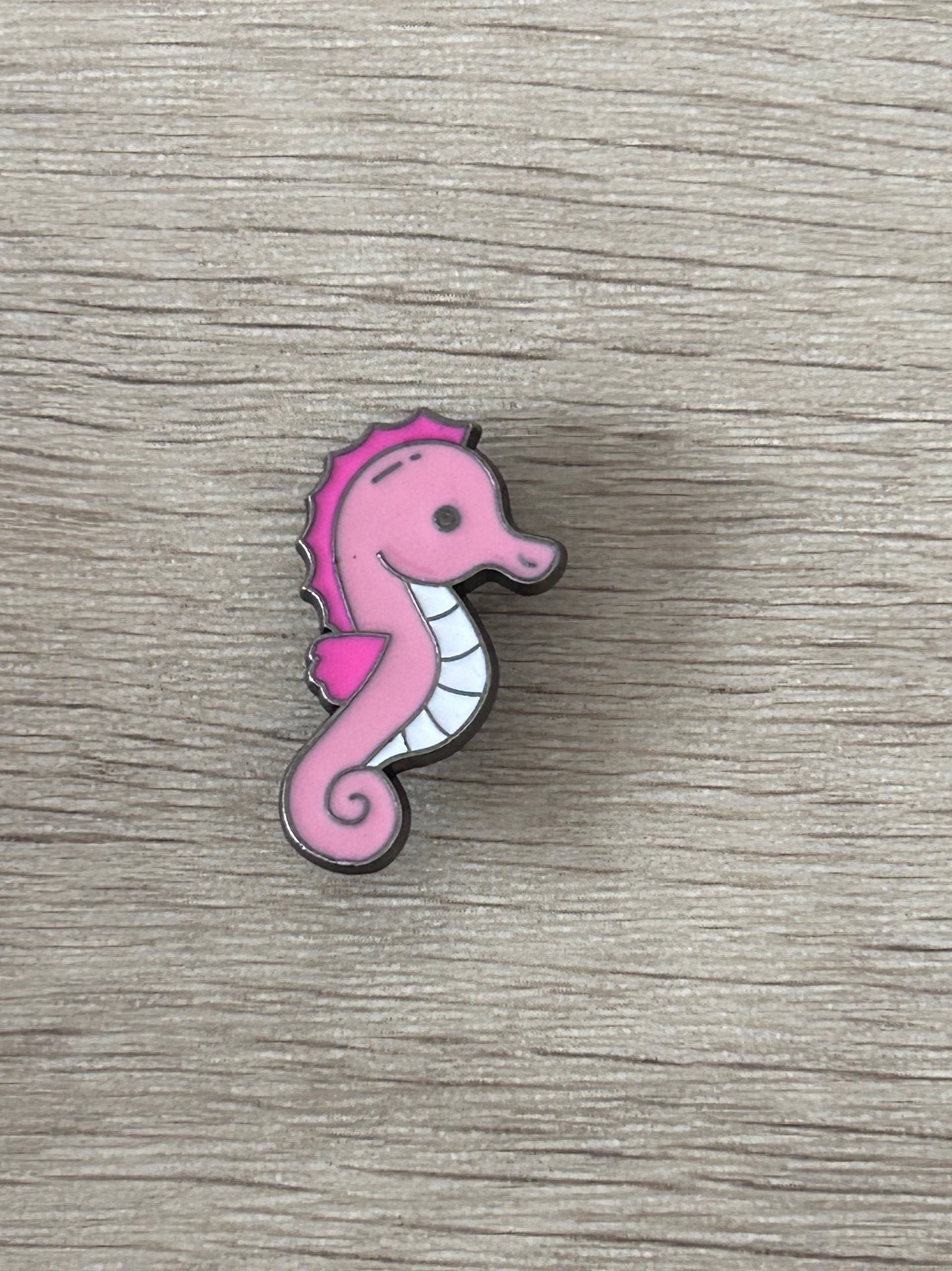 Pin hippocampe rose avec contour gris et ventre blanc.