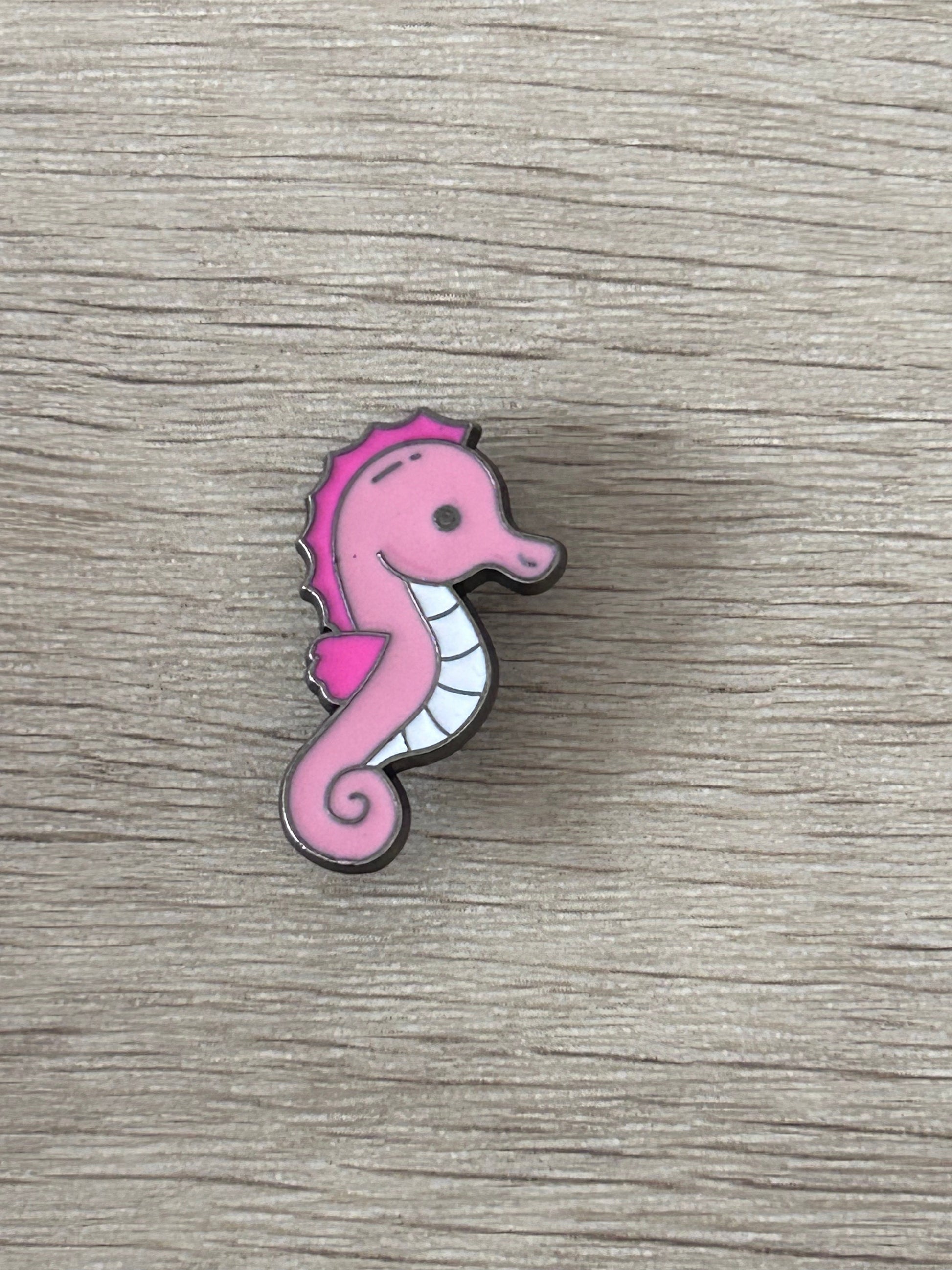 Pin hippocampe rose avec contour gris et ventre blanc.