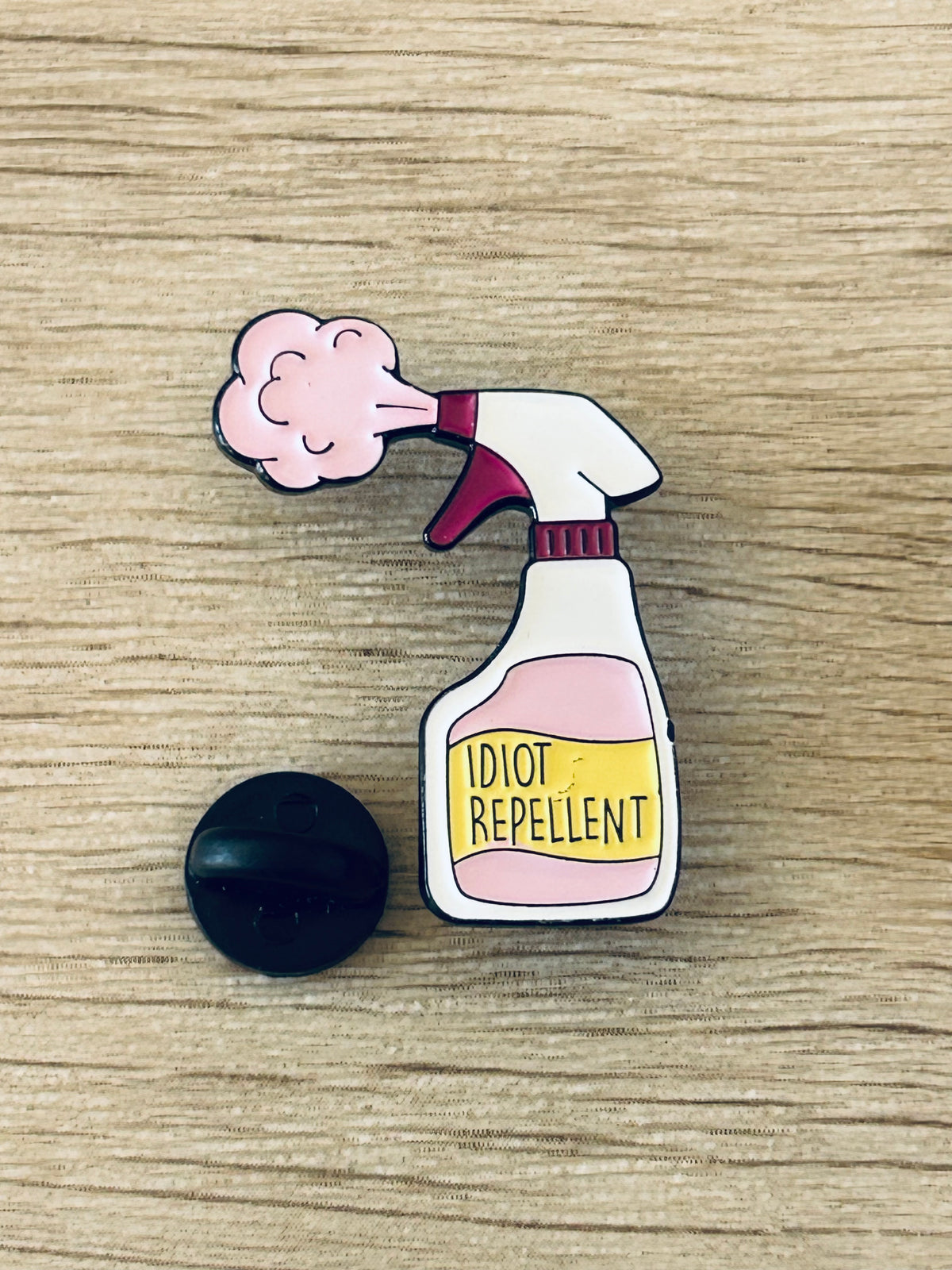 Goupille émaillée spray avec nuage rose et étiquette « IDIOT REPELLENT », avec capuchon noir