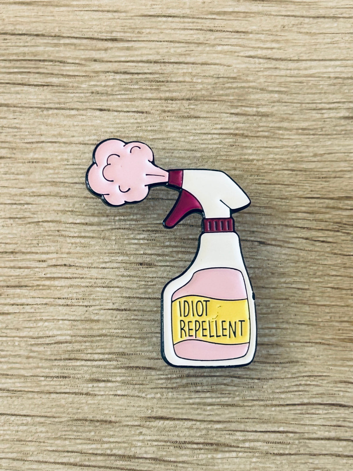 Goupille émaillée forme de spray, nuage rose et étiquette « IDIOT REPELLENT »