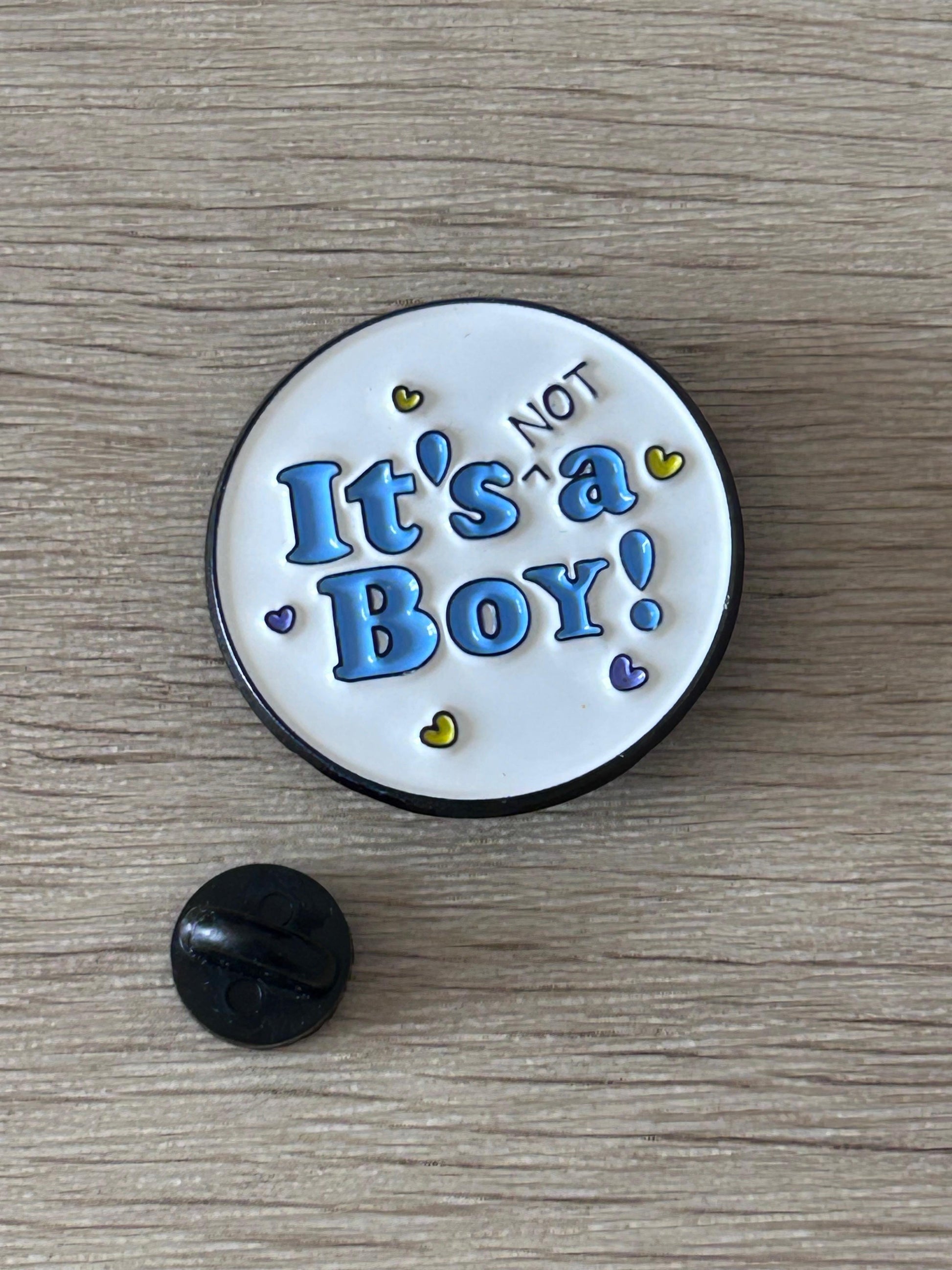 Pin's rond « It's NOT a Boy! » bleu, bord noir, avec attache noire.