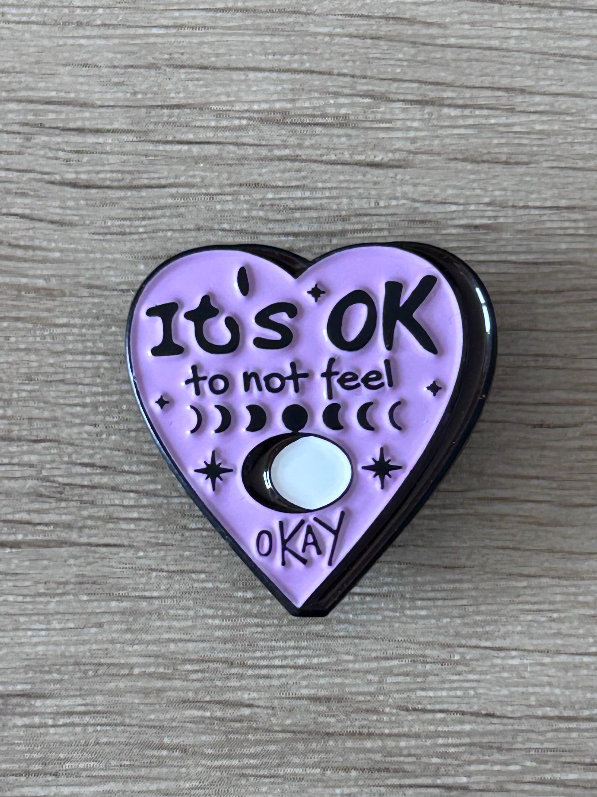 Pin cœur violet « It’s OK » avec texte et icône de lune.