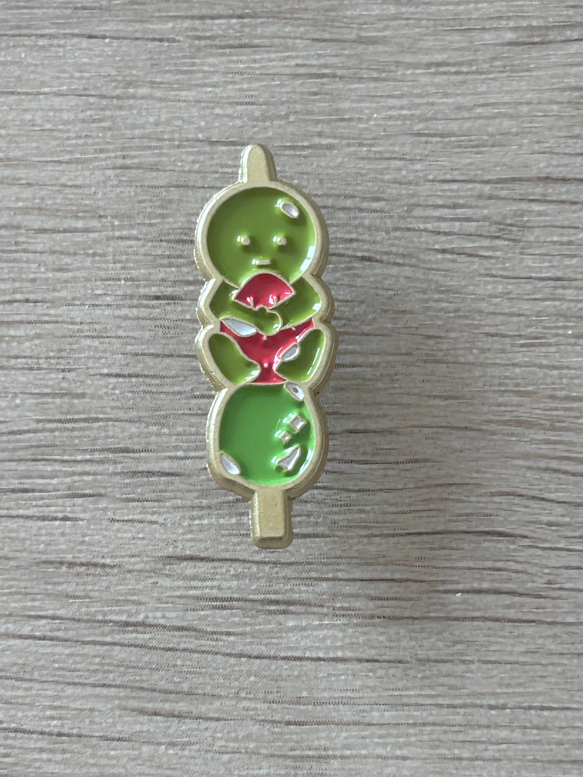 Pin émaillé vert en forme de personnage kawaii, détails rouges en forme de fraise