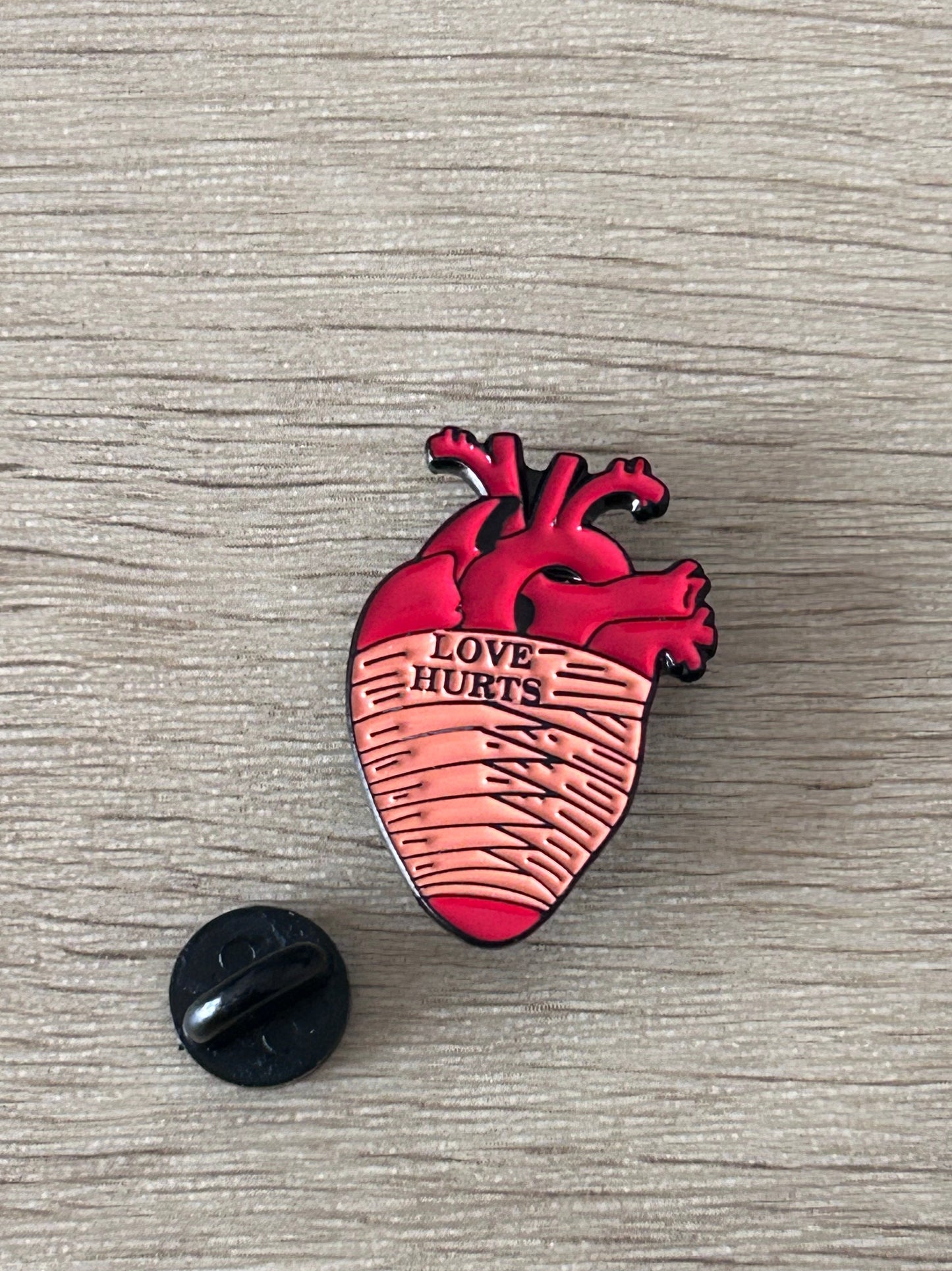 Pin cœur anatomique rouge, lignes façon ECG et texte « Love Hurts »