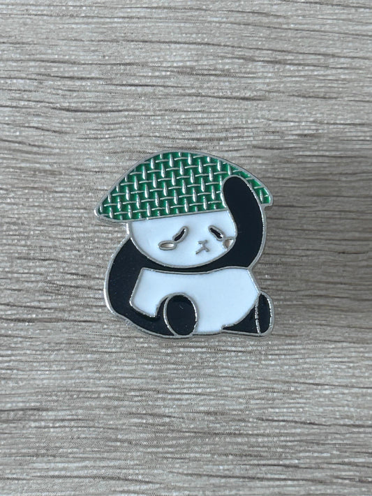 Broche panda avec chapeau de paille vert tissé, visage blanc et corps noir.