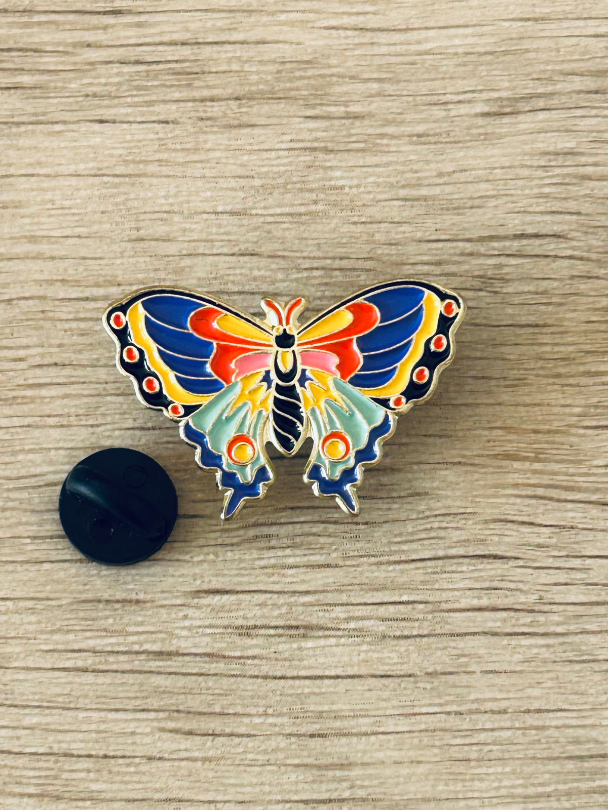 Broche papillon émaillée multicolore avec pastille noire assortie.