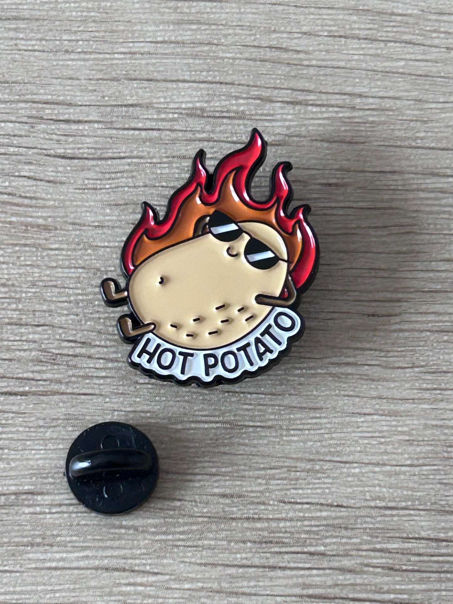 Épingle émaillée patate en flammes avec inscription HOT POTATO et attache noire.